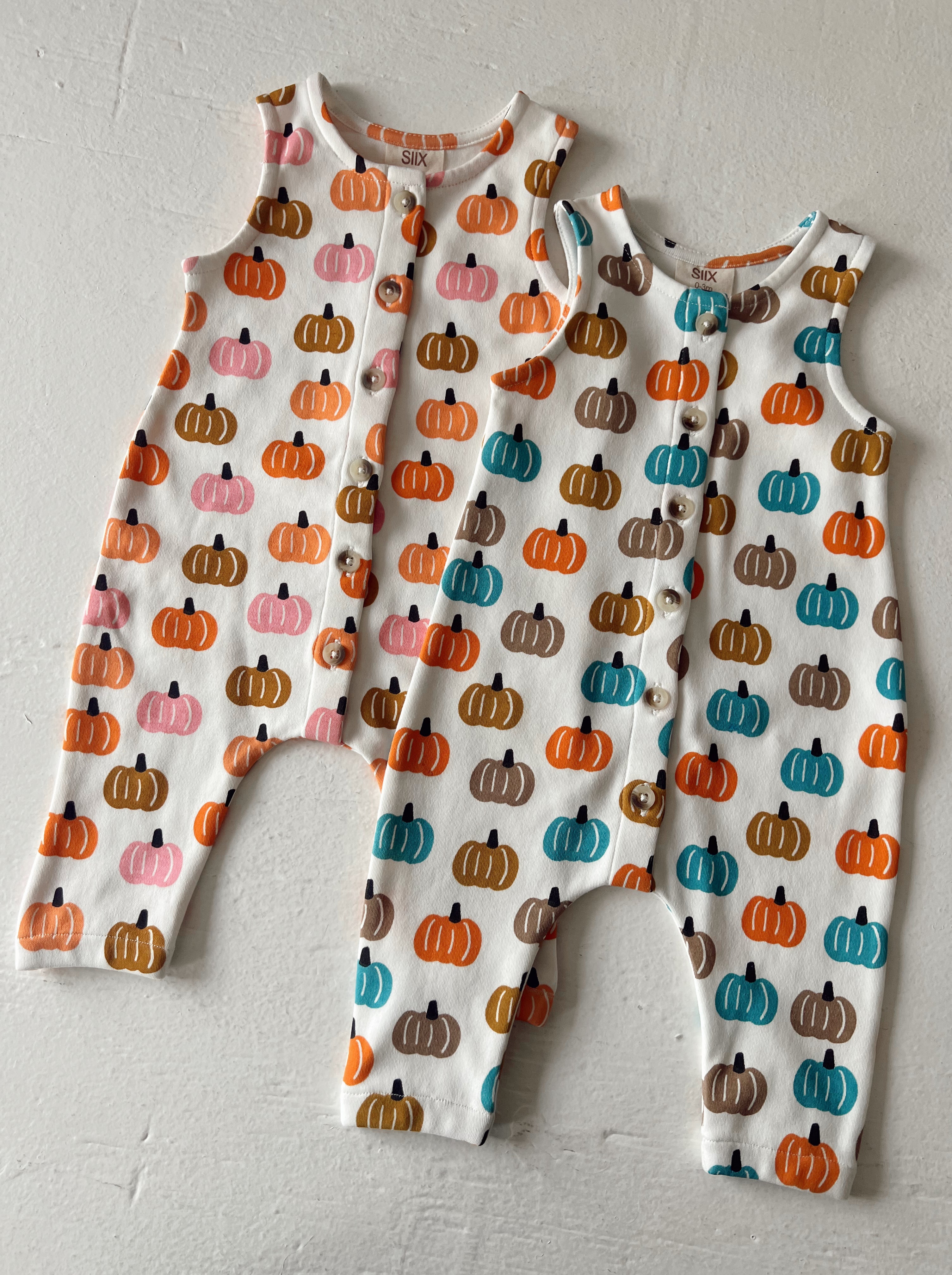 Two baby rompers with colorful pumpkin patterns on a white background, displayed on a light surface.