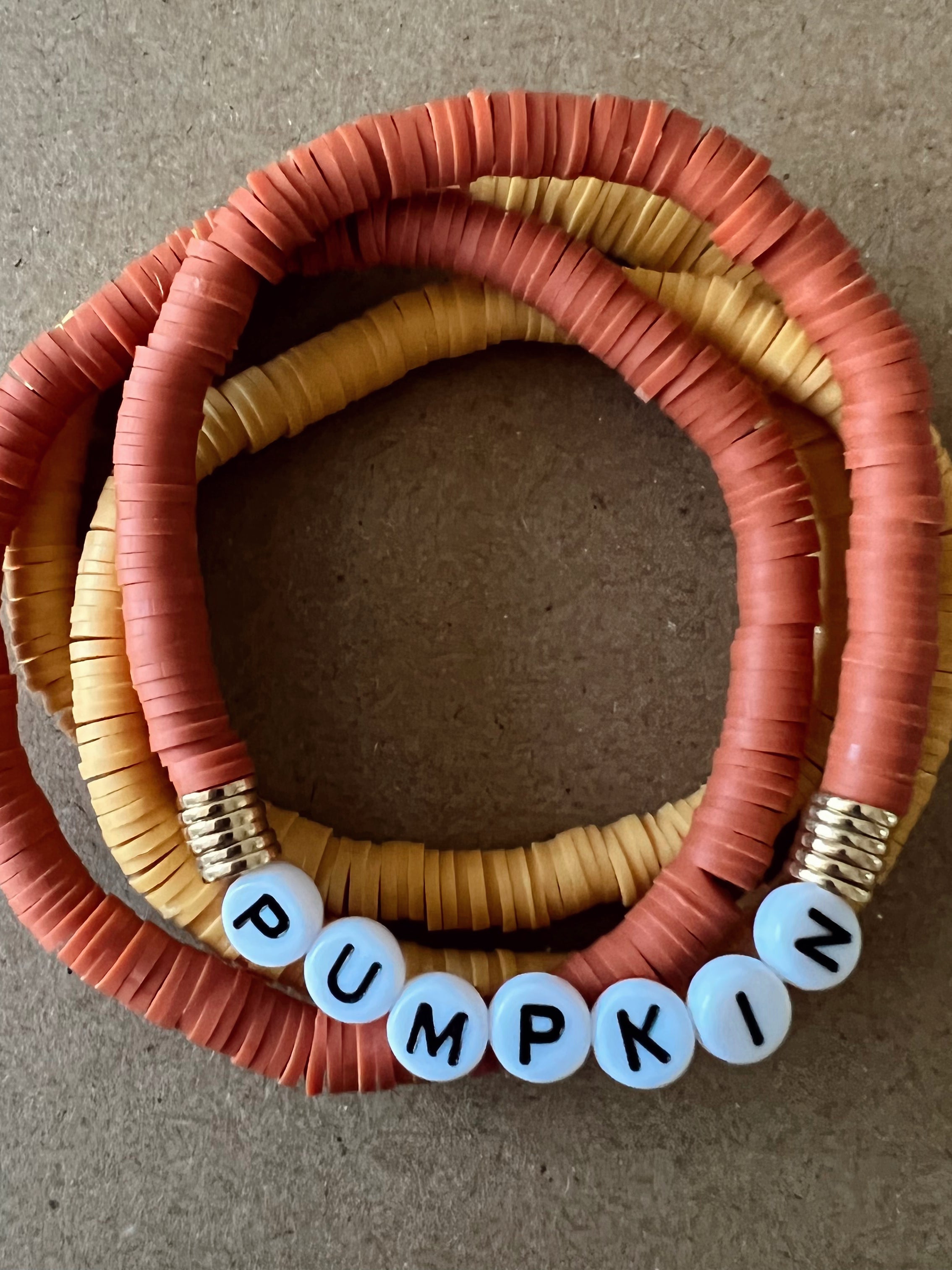 Colorful beaded bracelets in orange and yellow, featuring the word "PUMPKIN" spelled out in letter beads.