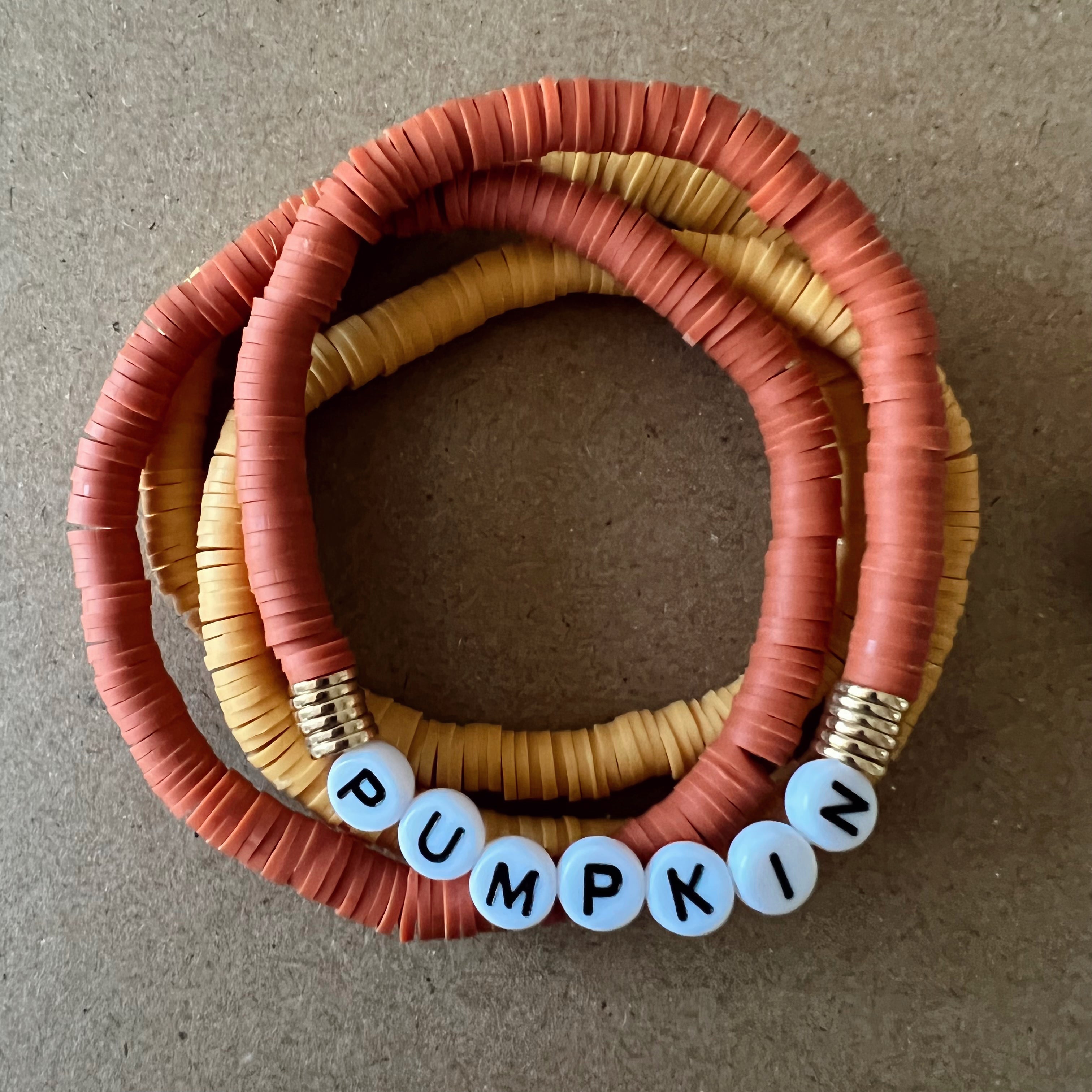 Colorful beaded bracelets in orange and yellow, featuring the word "PUMPKIN" spelled out in letter beads.