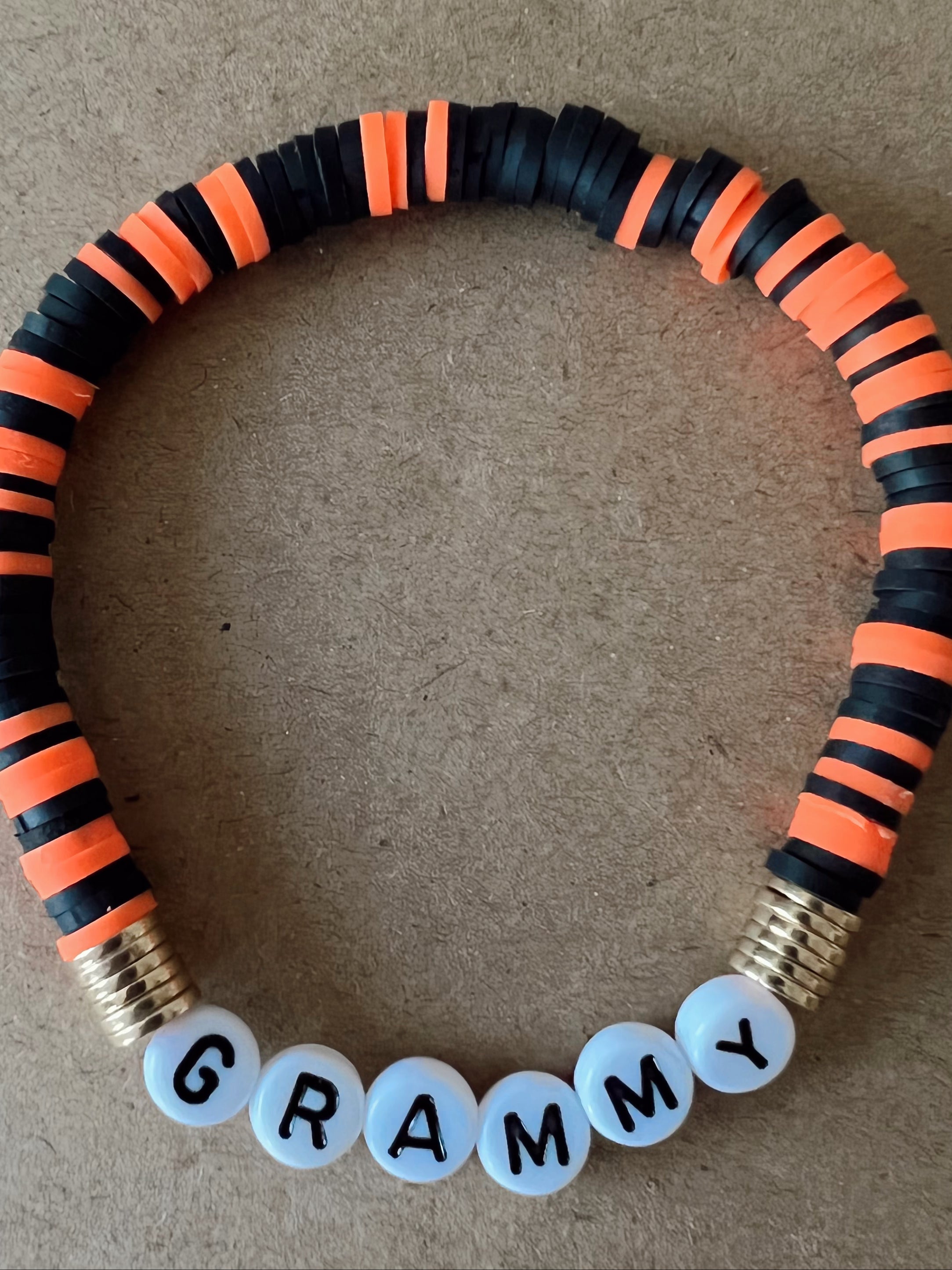 Colorful bracelet made of black and orange beads, featuring white beads that spell "GRAMMY."