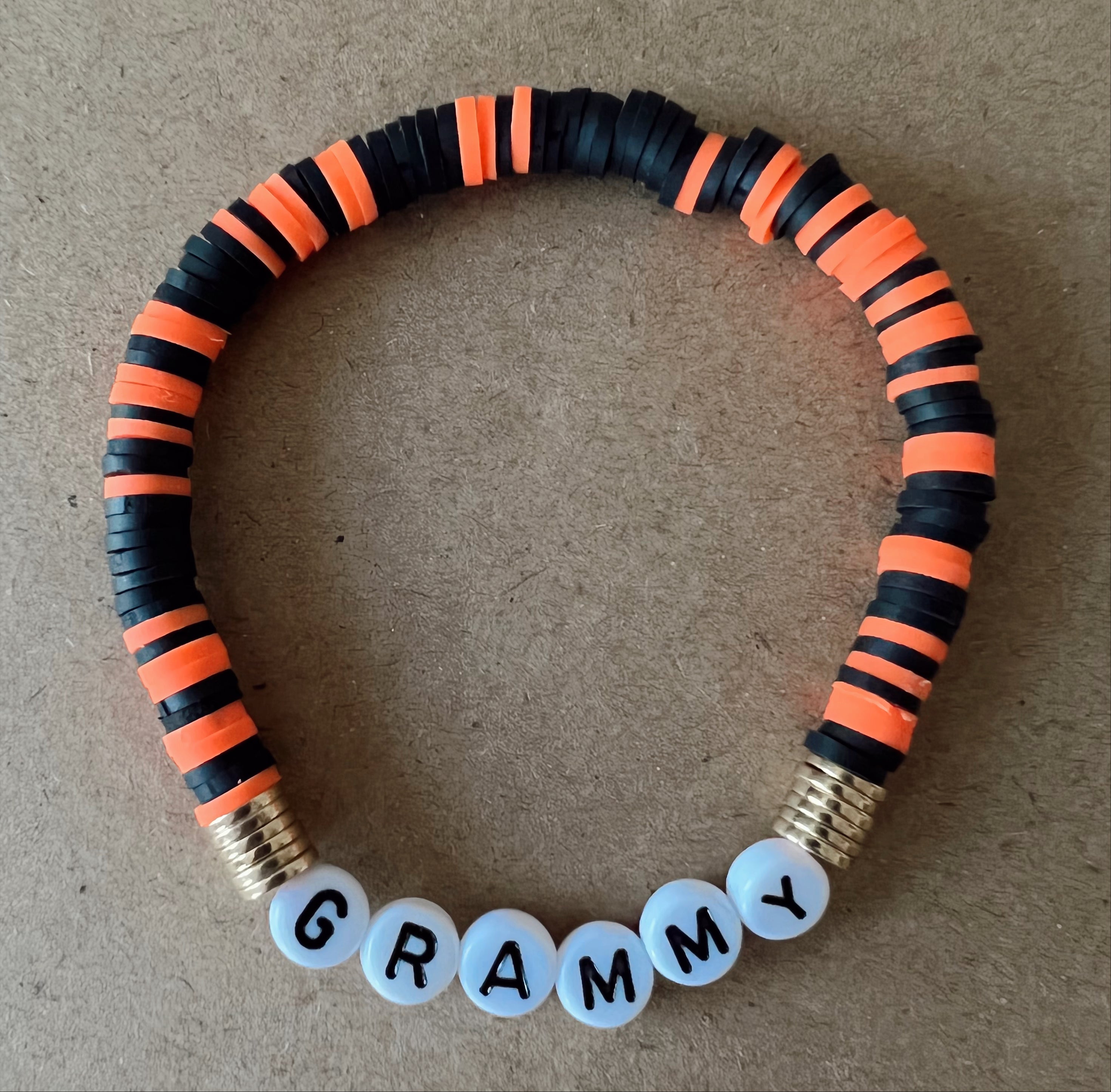 Colorful bracelet made of black and orange beads, featuring white beads that spell "GRAMMY."
