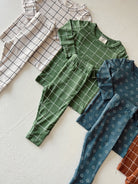 Assorted children's outfits in green, blue, and cream with patterned tops and pants laid flat on a light background.