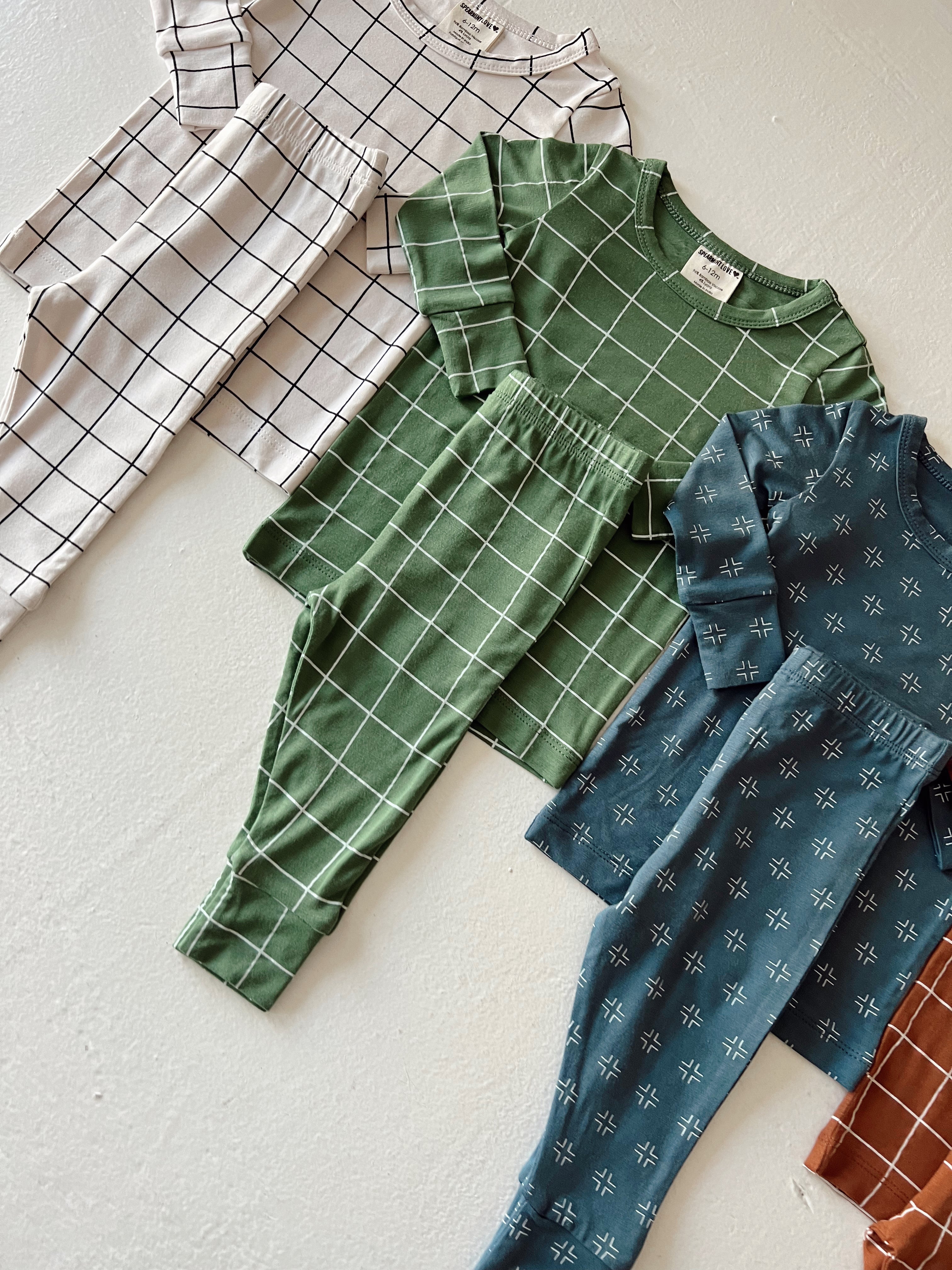 Assorted children's outfits in green, blue, and cream with patterned tops and pants laid flat on a light background.