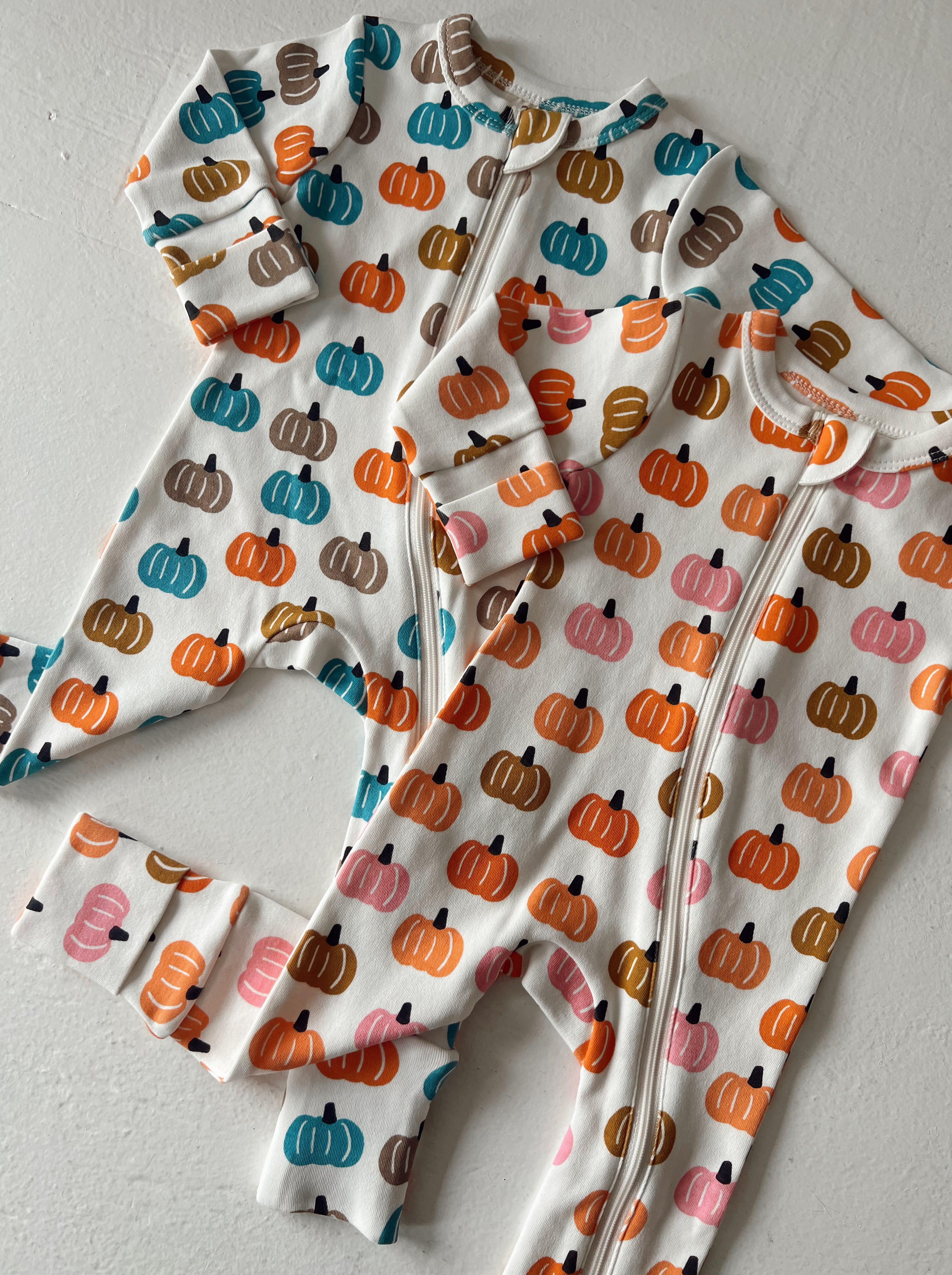 Two infant onesies with colorful pumpkin patterns on a light background.