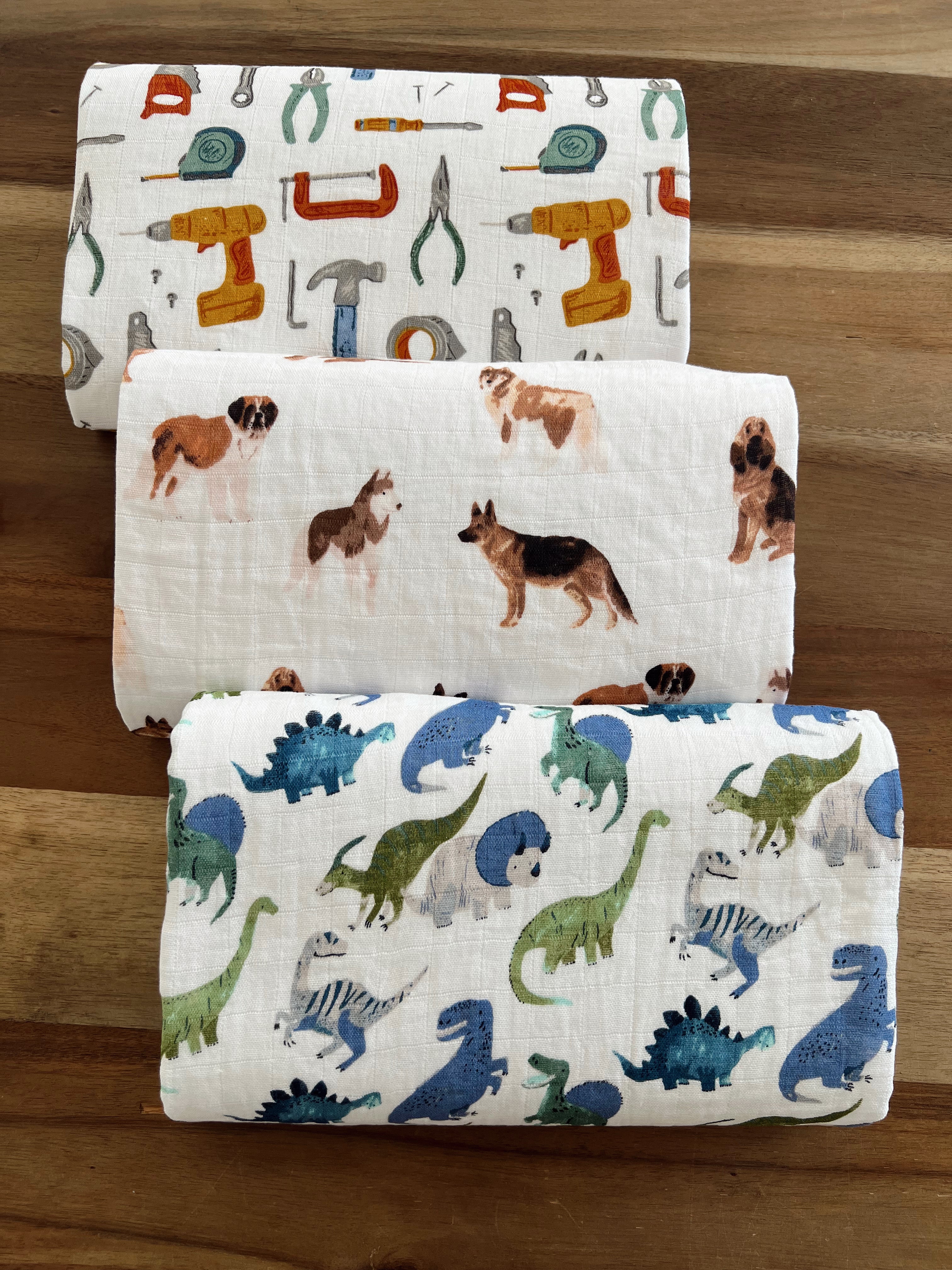Three patterned fabric rolls featuring tools, dogs, and dinosaurs on a wooden surface.