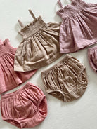 Assorted infants' linen tops and shorts in soft pink and beige hues on a light background.