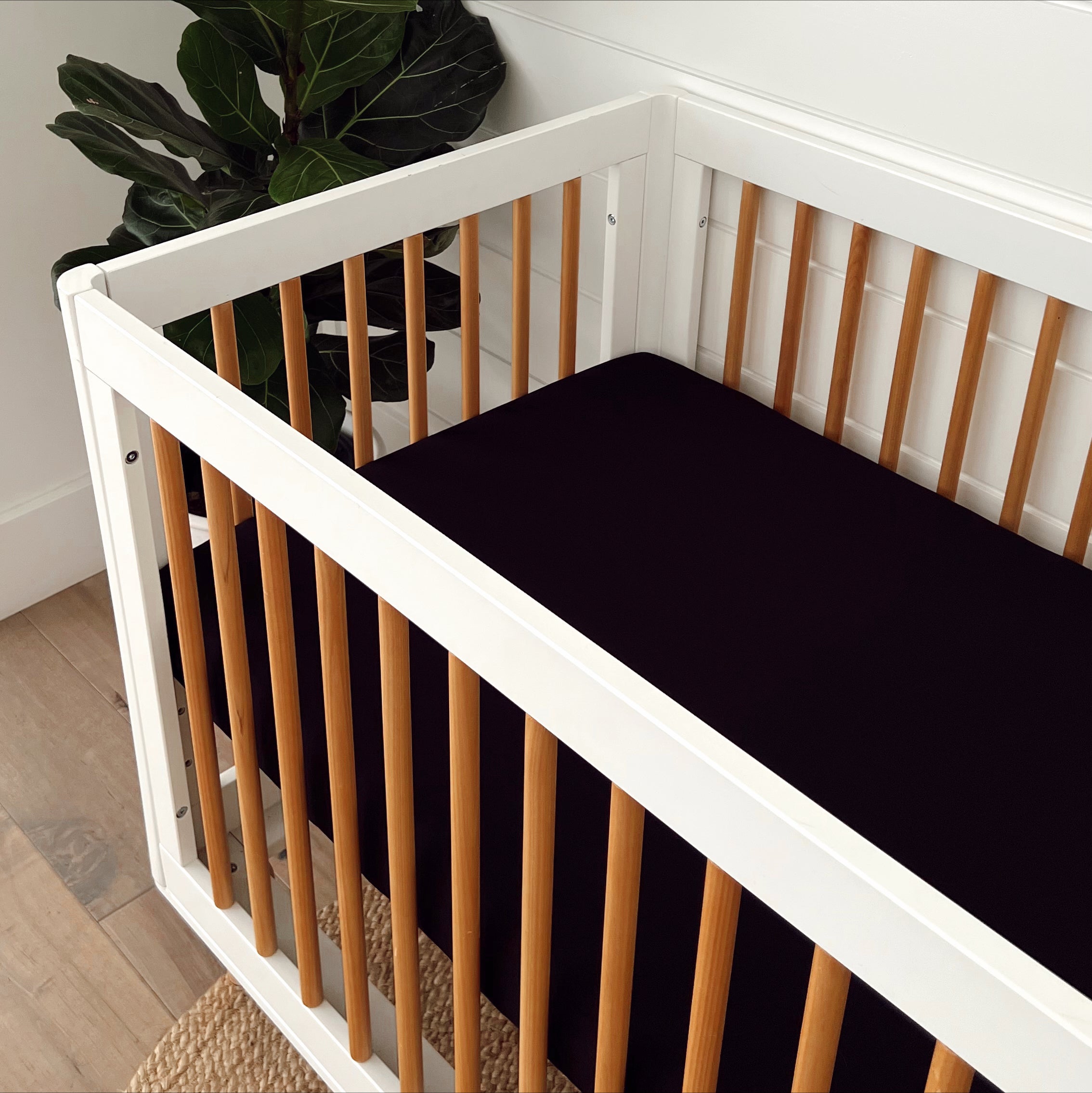 Modern crib with wooden slats and a dark mattress, surrounded by indoor plants and natural light.