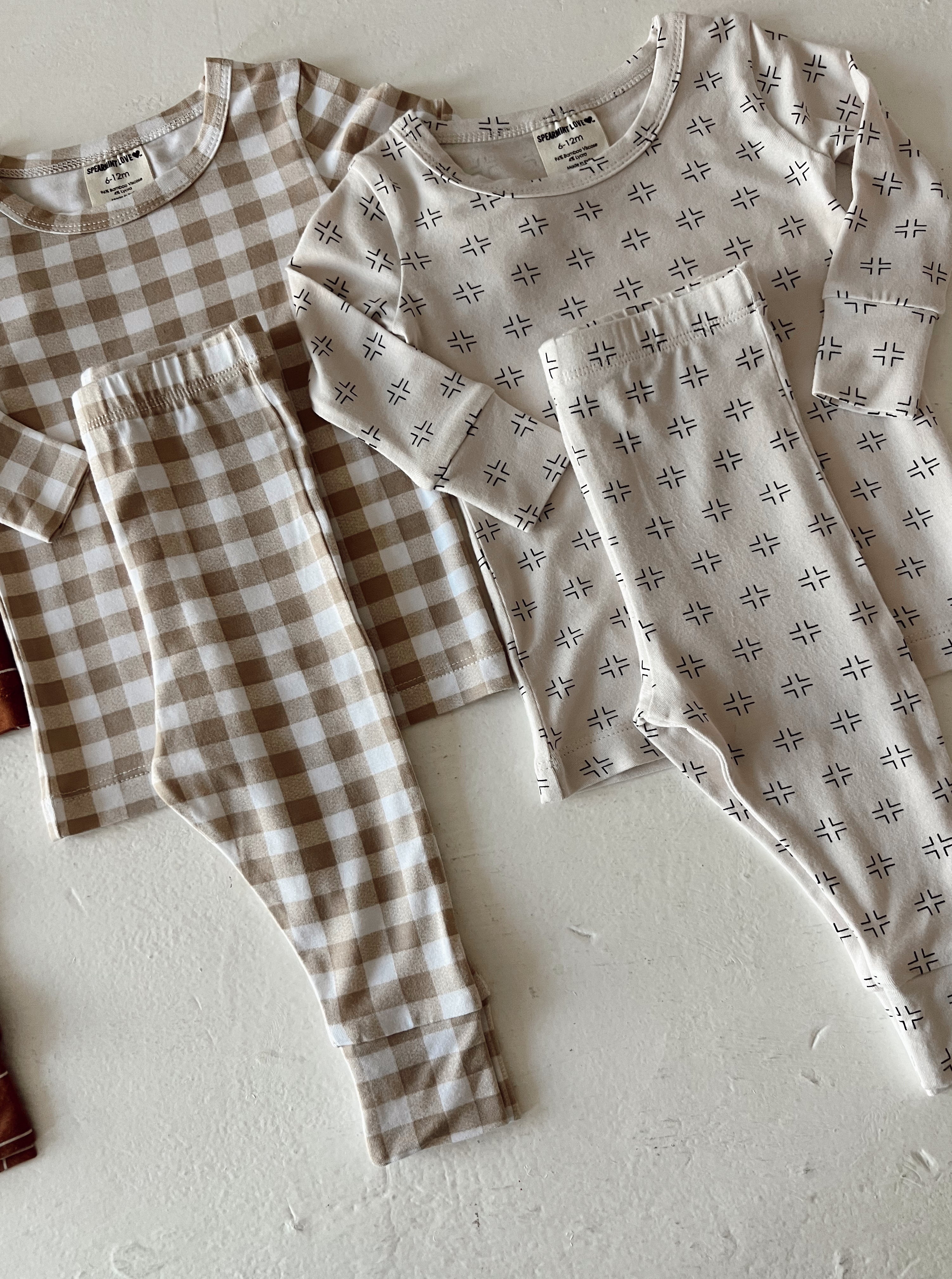 Two sets of matching children's pajamas in neutral colors and patterns, laid out on a textured surface.