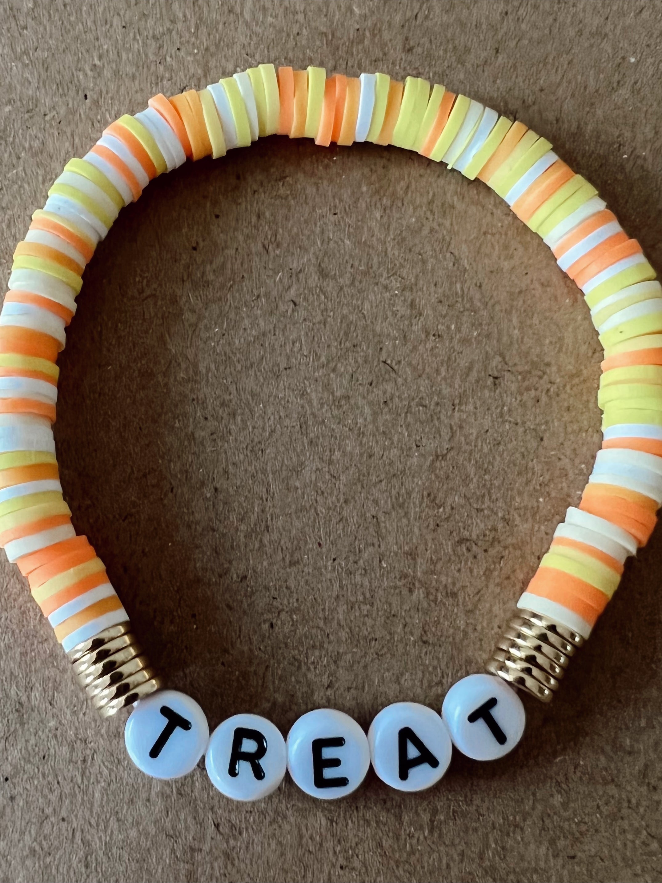 Colorful bead bracelet with the word "TREAT" spelled out in white beads, set against a brown background.