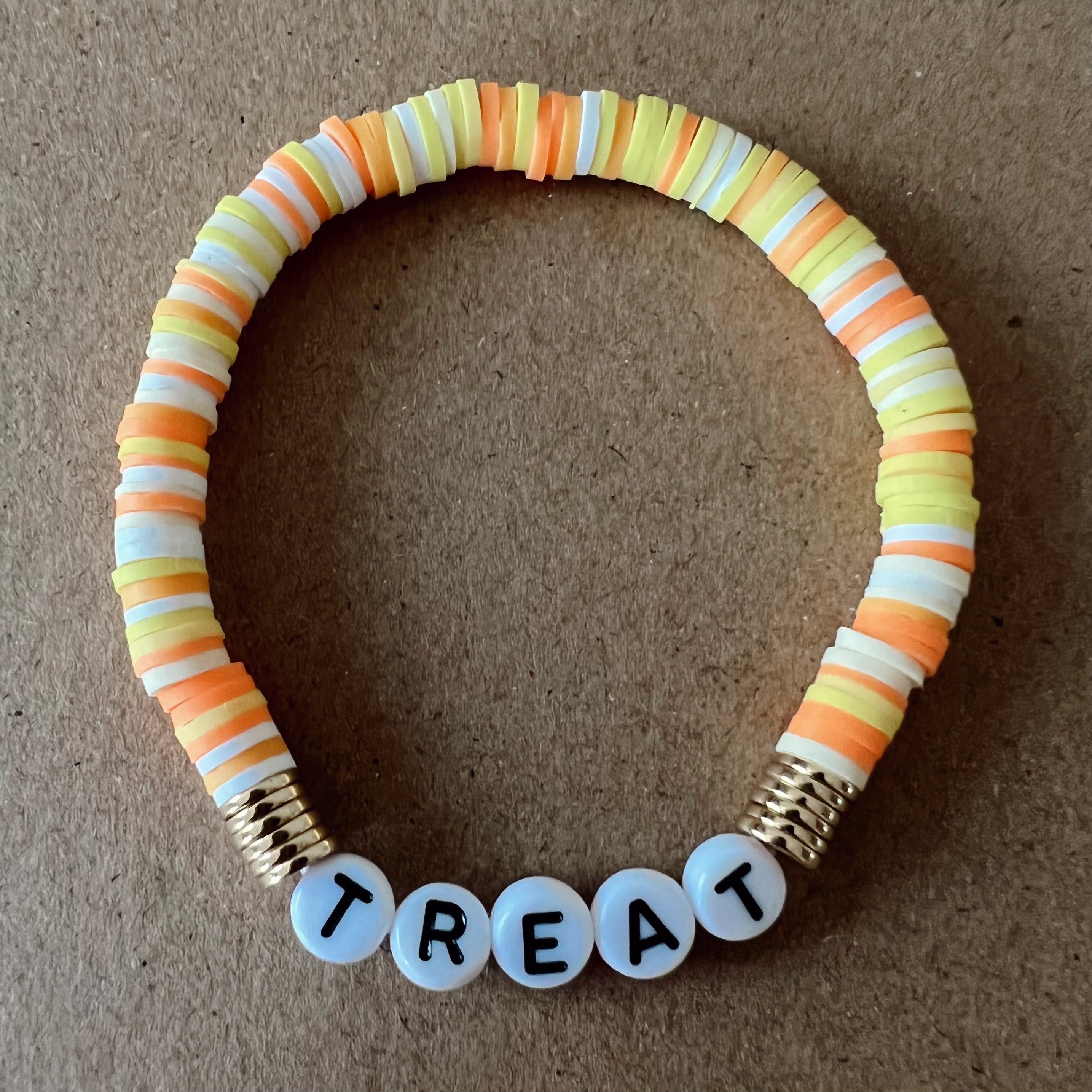 Colorful bead bracelet with the word "TREAT" spelled out in white beads, set against a brown background.