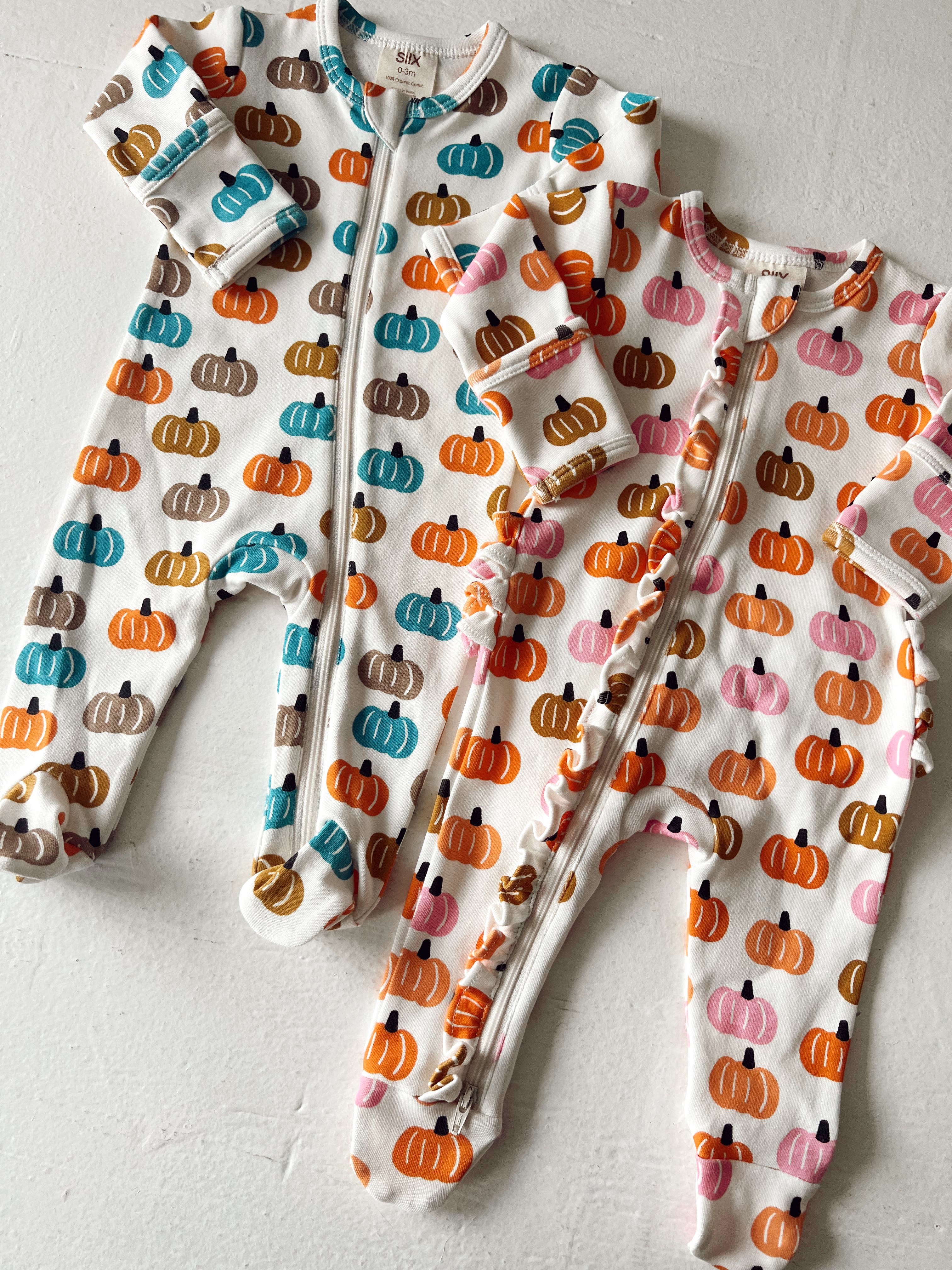 Two children's onesies with colorful pumpkin patterns, one in teal and orange, the other in pink and orange.