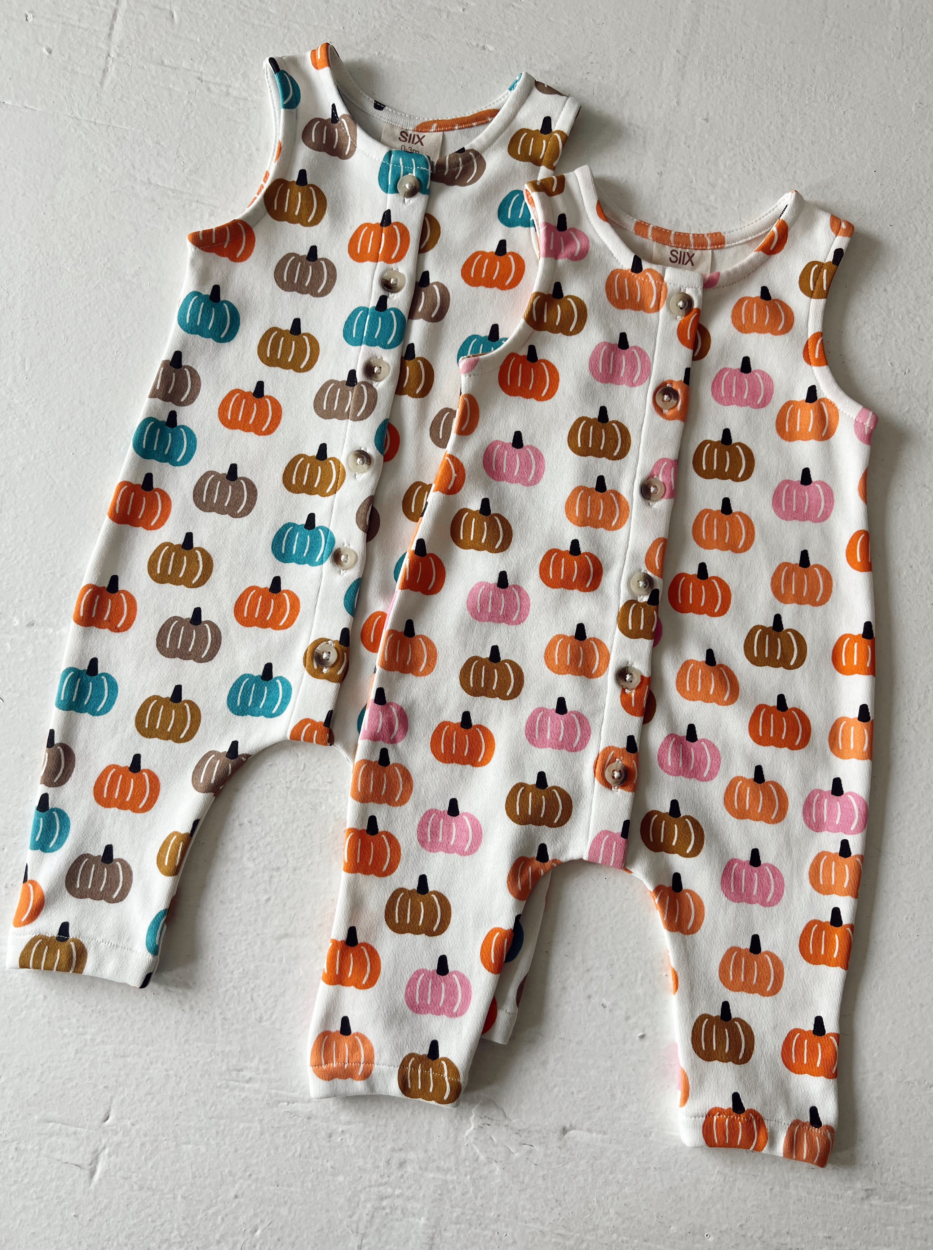 Two colorful pumpkin-patterned baby rompers with buttons, displayed on a light background.