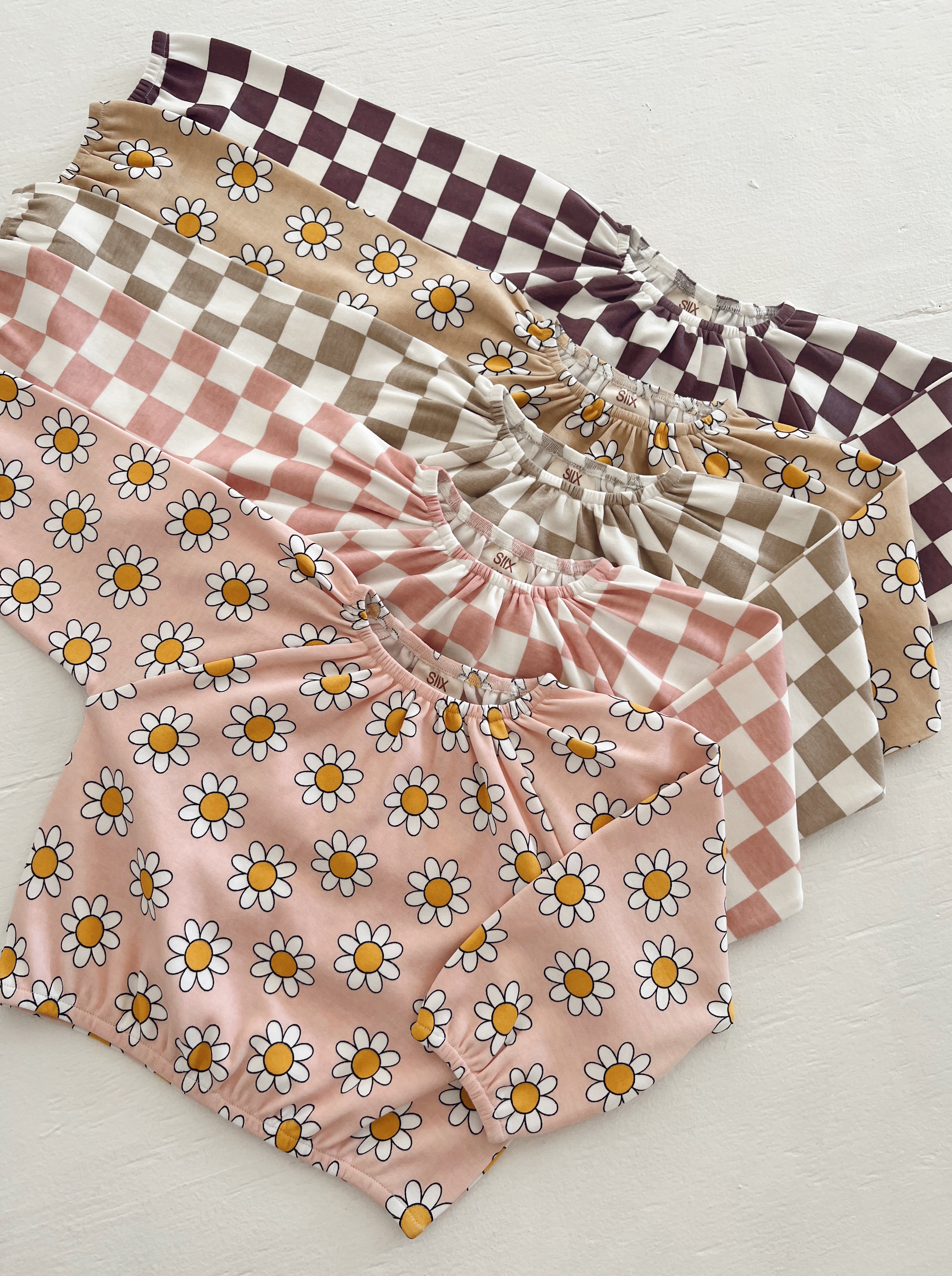 Assorted children's clothing featuring floral and checkered patterns in pastel colors.