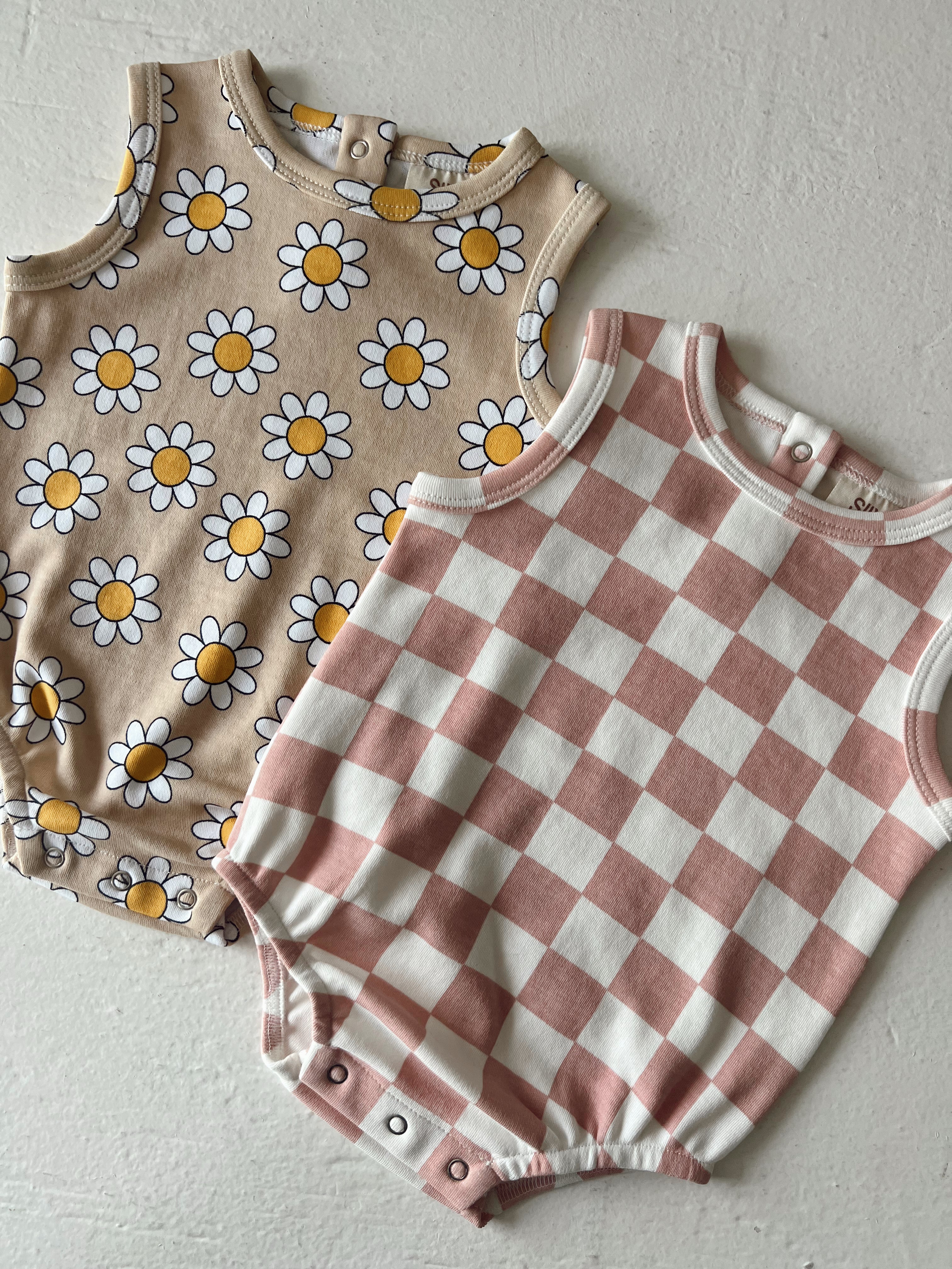Two baby onesies: one with a daisy pattern and the other in a pink and white checkered design.