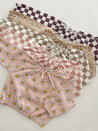 Colorful children's tops with floral and checkered patterns stacked on a light background.