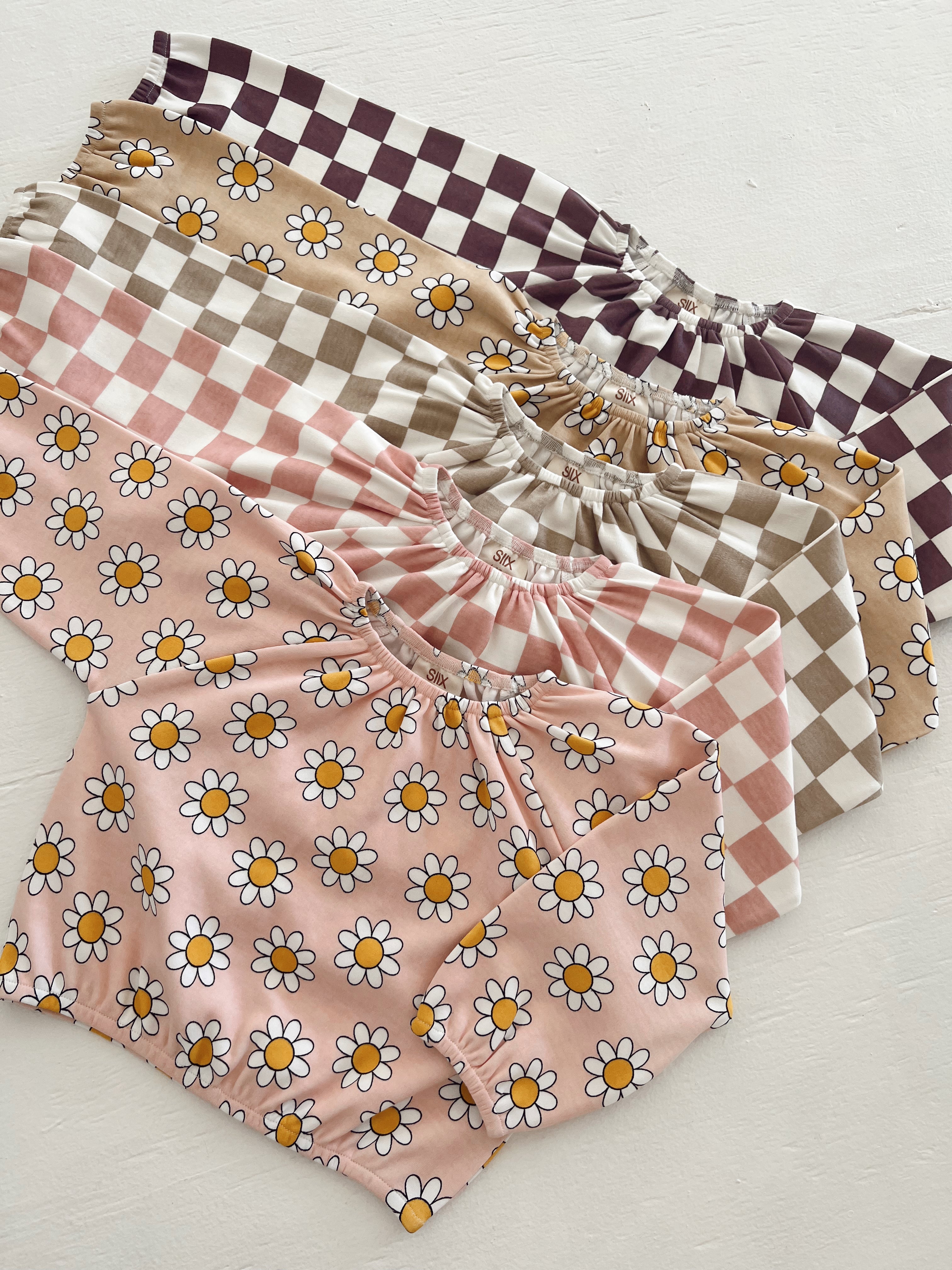 Colorful children's tops with floral and checkered patterns stacked on a light background.