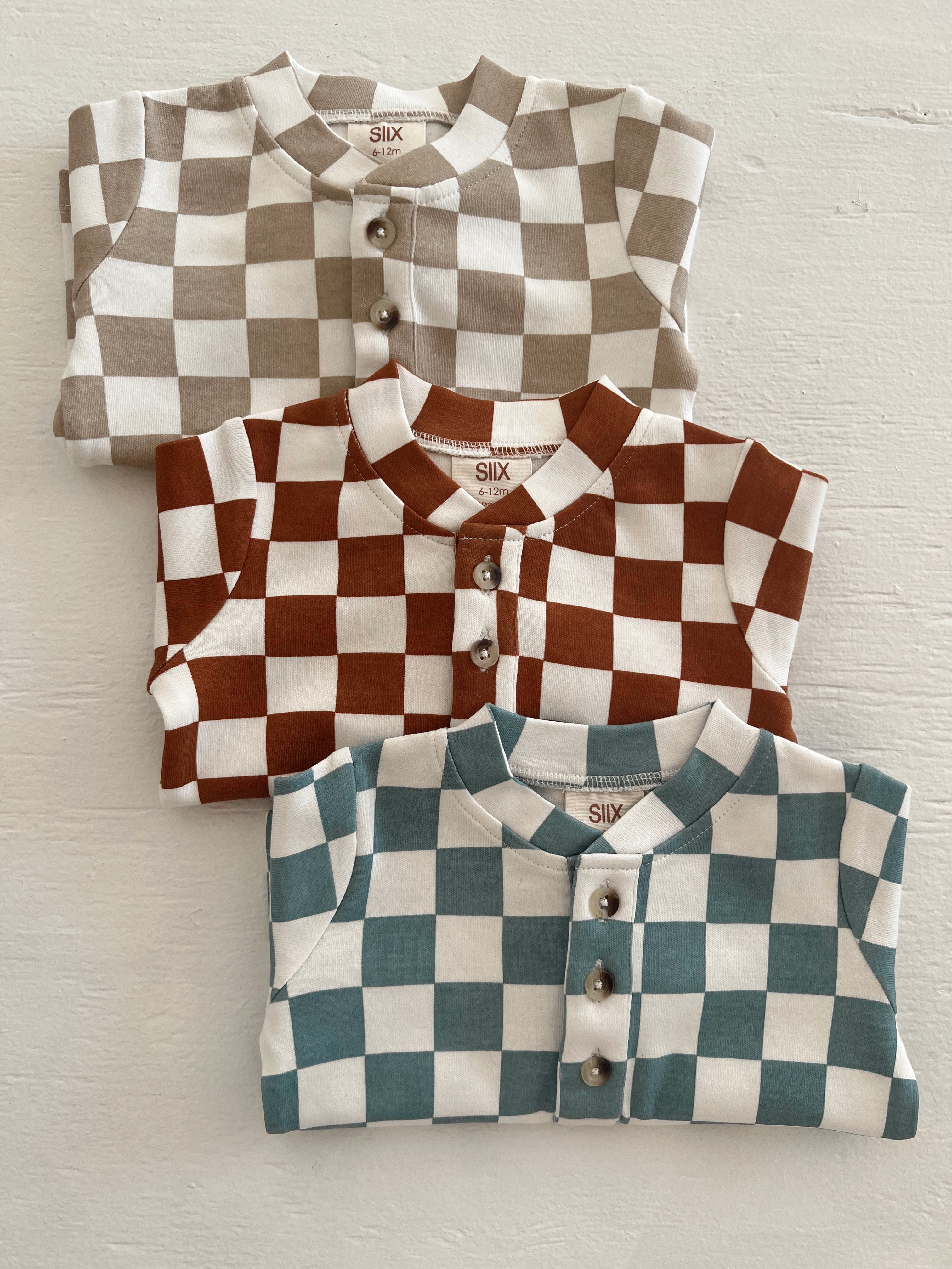 Three folded baby shirts with checkerboard patterns in brown, teal, and beige hues, featuring button closures.