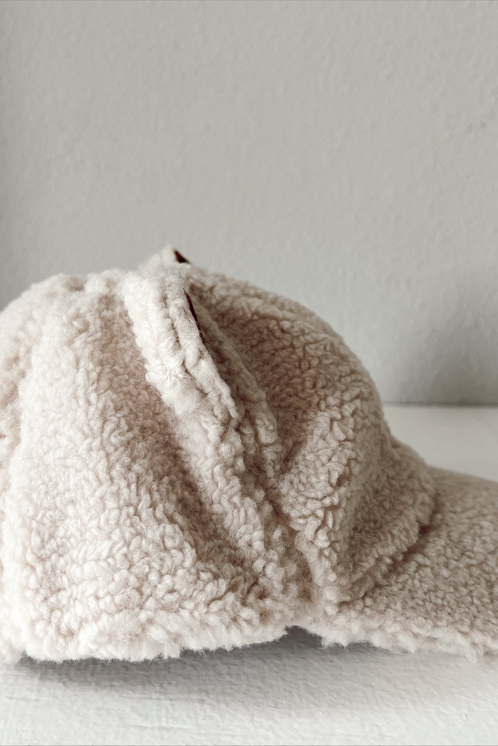 Side view of a soft beige furry cap resting on a white surface.