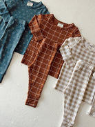 Three sets of children's outfits: teal, brown checkered, and beige plaid, displayed on a light background.