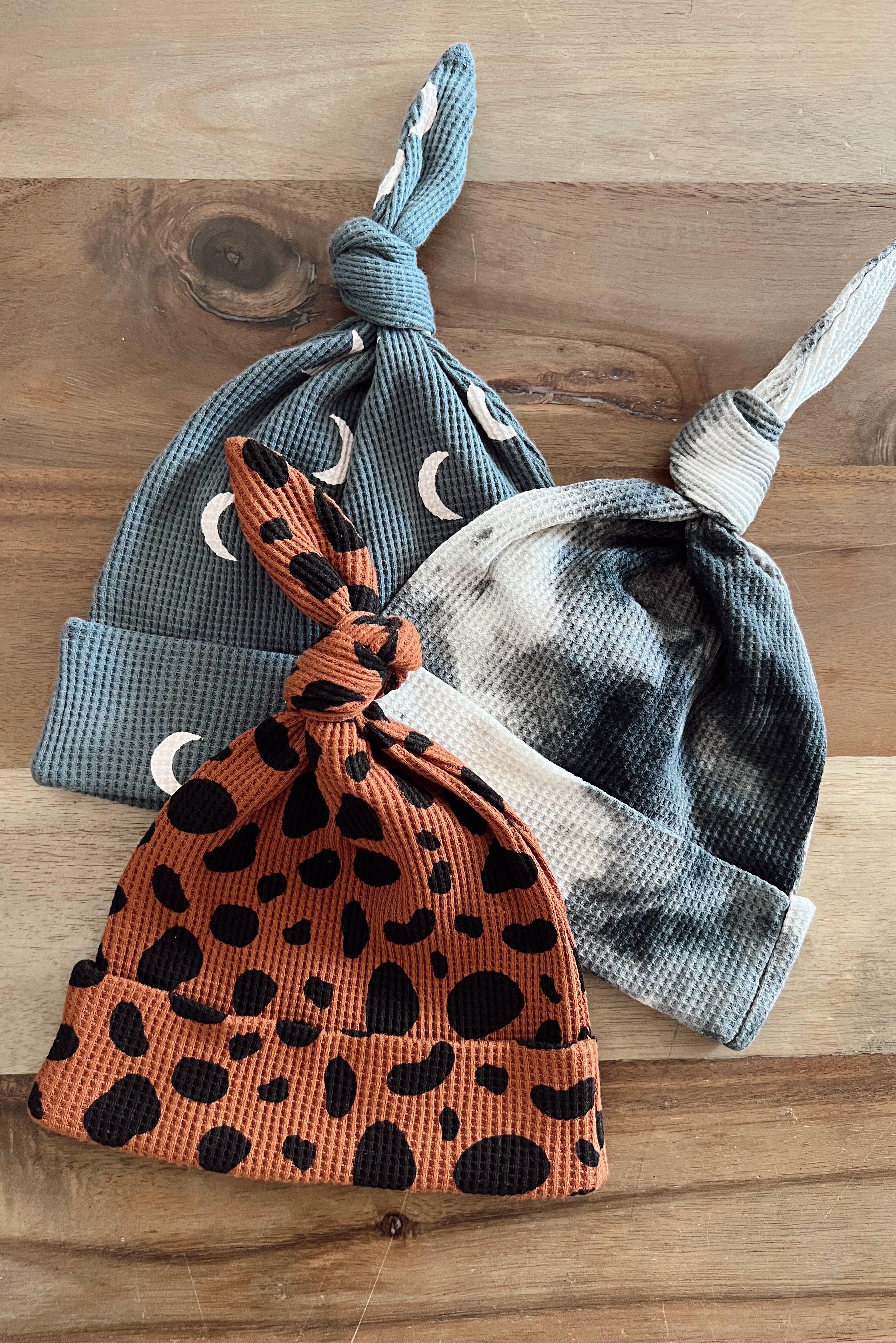 Three distinct baby hats in various colors and patterns, displayed on a wooden surface.