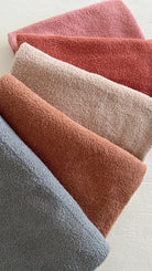 Texture-rich towels in soft shades of gray, pink, and red arranged neatly on a light surface.