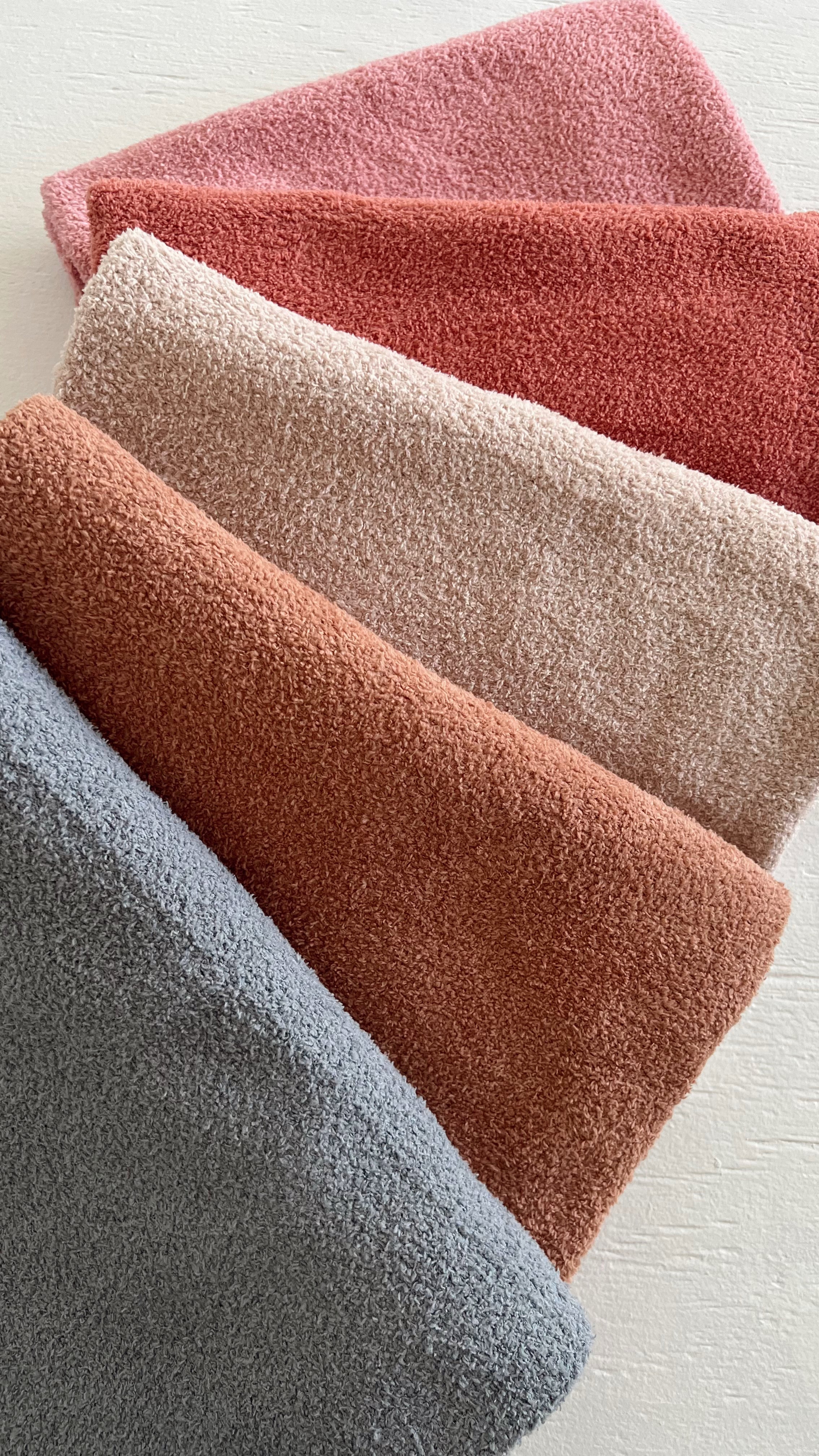 Texture-rich towels in soft shades of gray, pink, and red arranged neatly on a light surface.