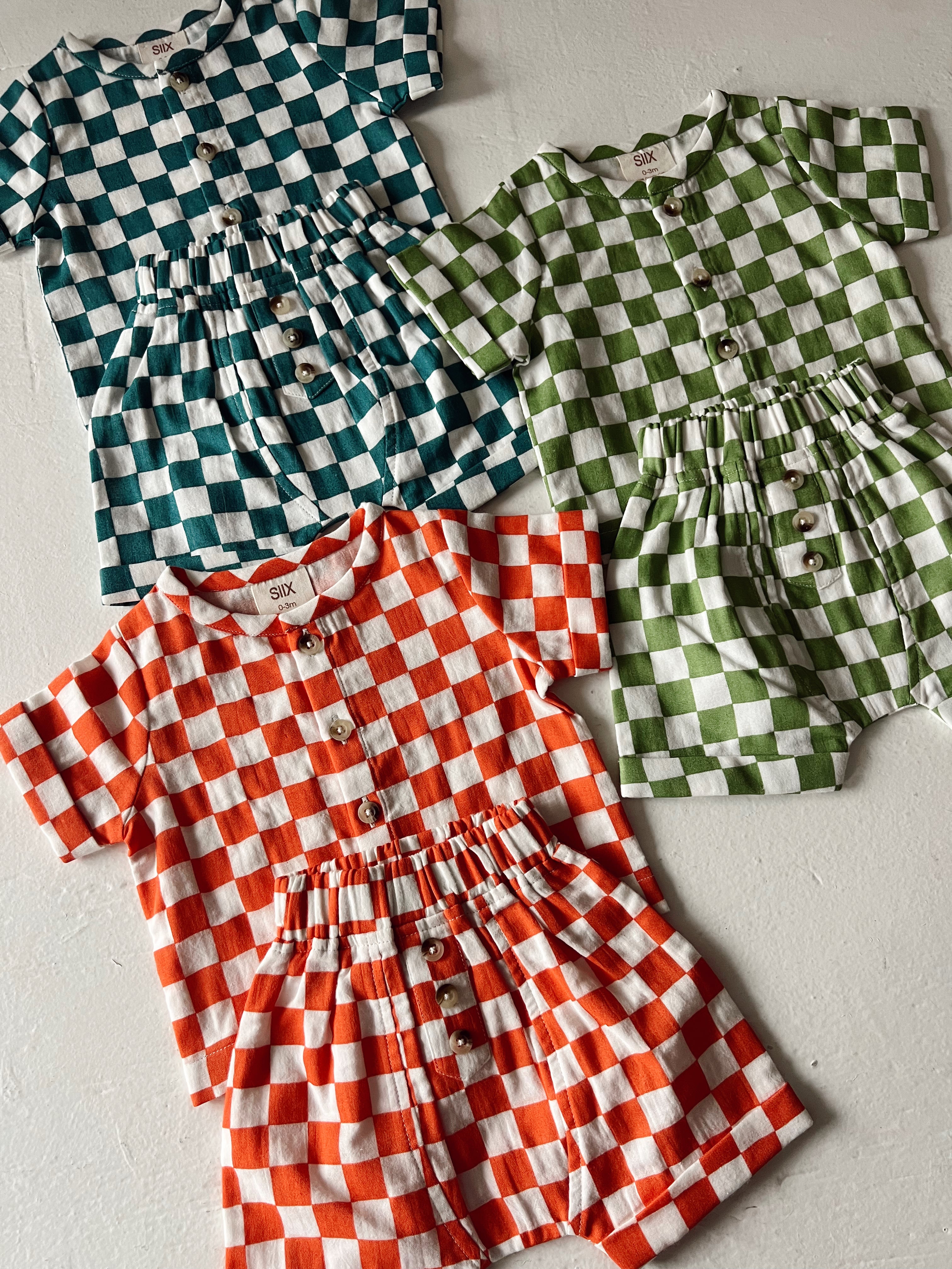 Four checkered outfits in red, green, teal, and white, featuring buttons and elastic waistbands.