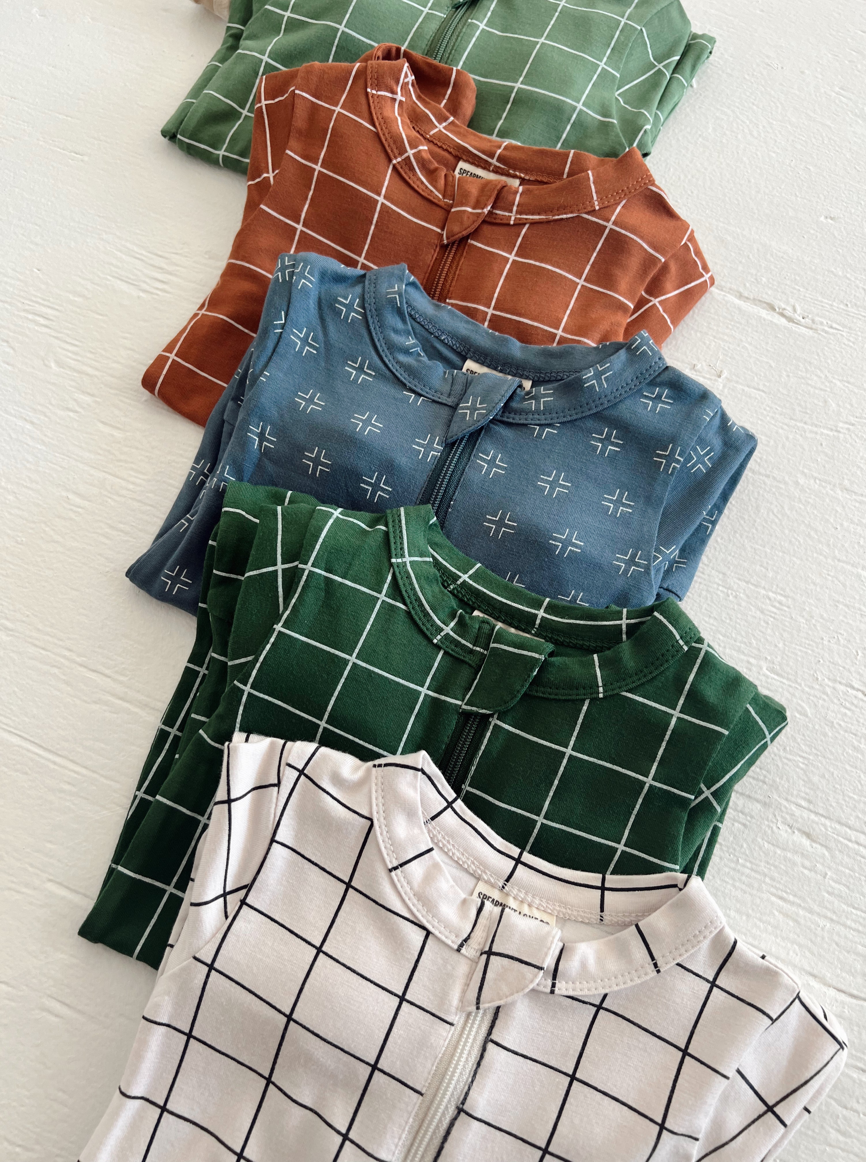 Five colorful, grid-patterned toddler outfits stacked neatly on a white surface.