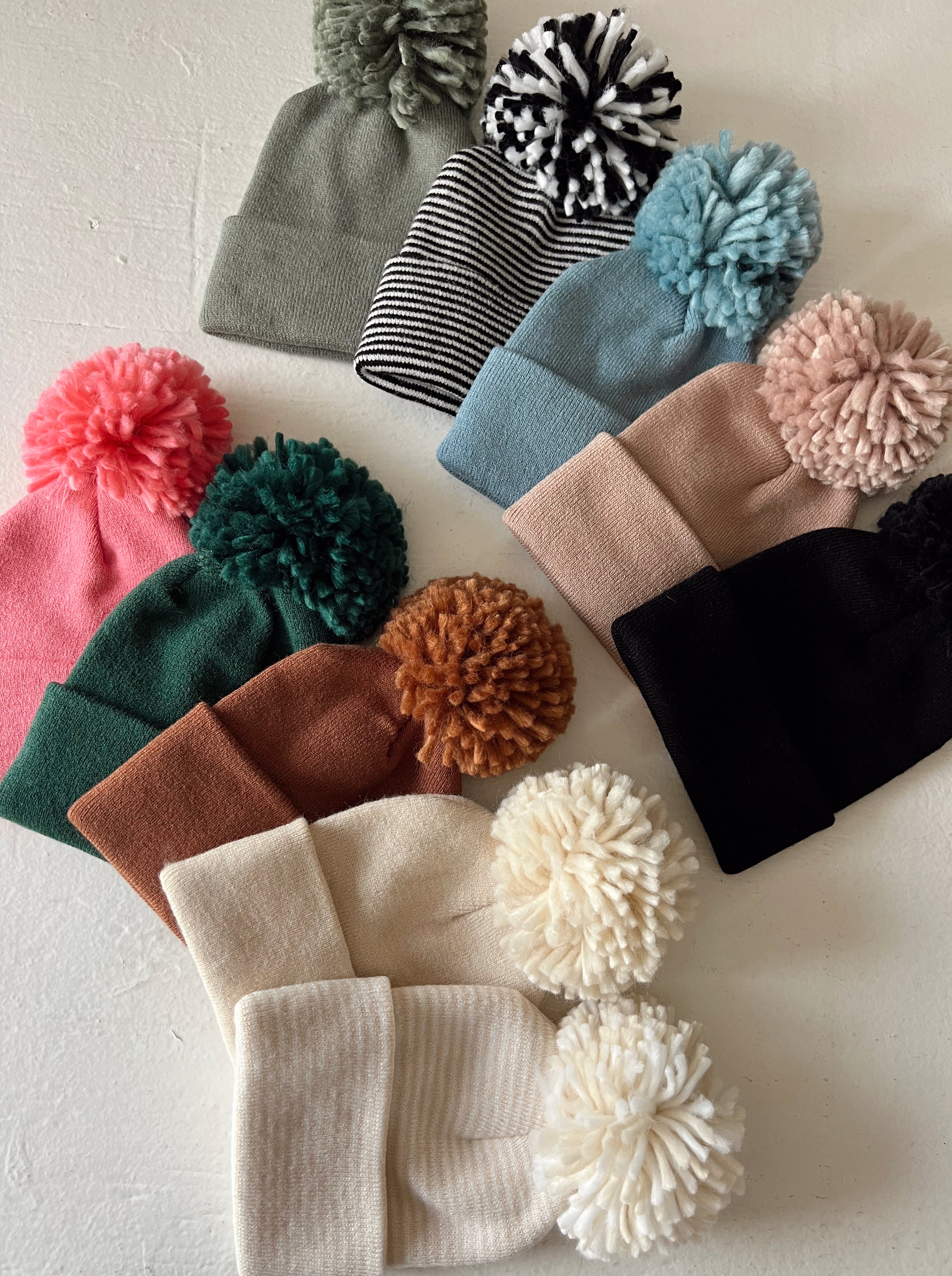 Colorful winter beanies with pom-poms arranged on a light background.