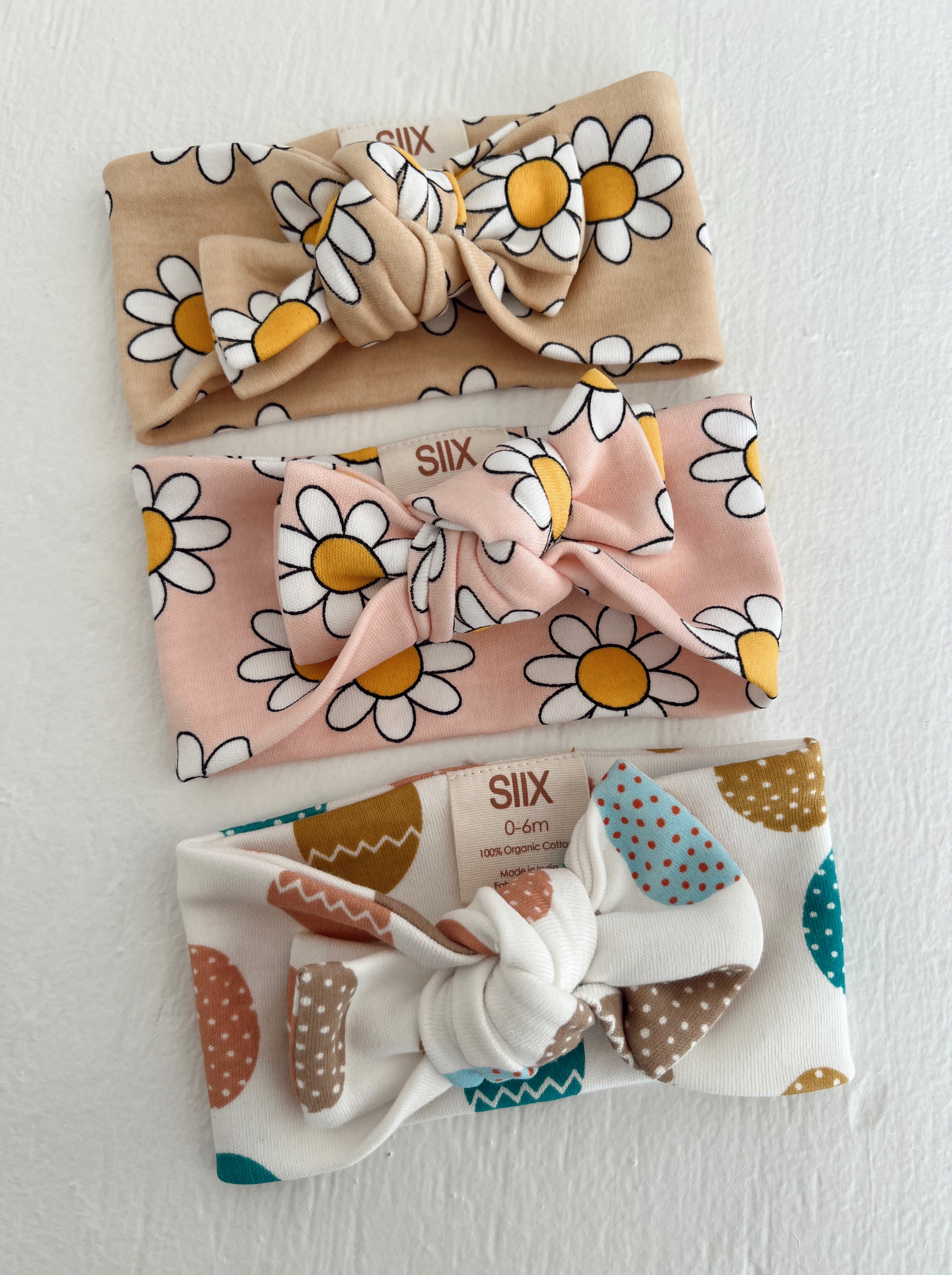 Three baby headbands in floral and patterned designs: beige daisy, pink daisy, and colorful polka dot.