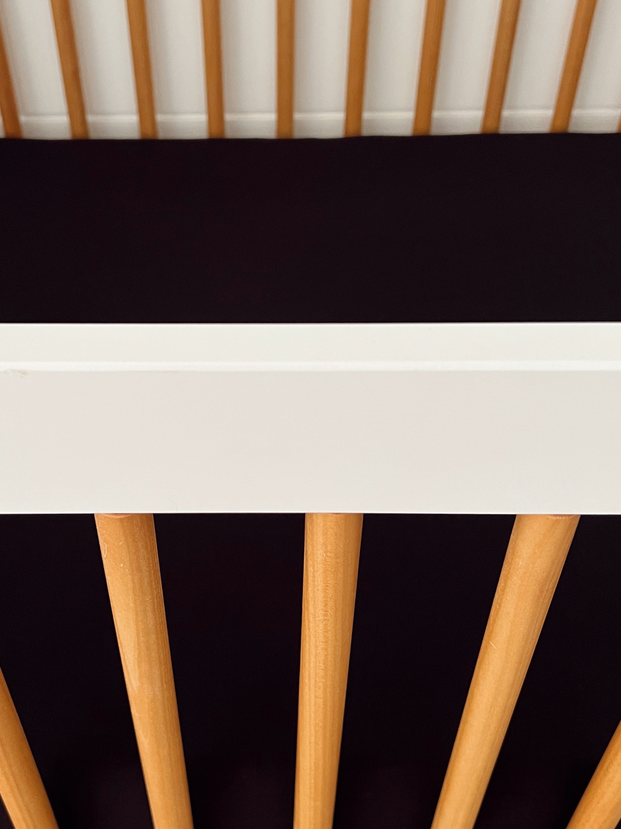 Close-up of a crib showing wooden rods and a white top rail against a dark background.