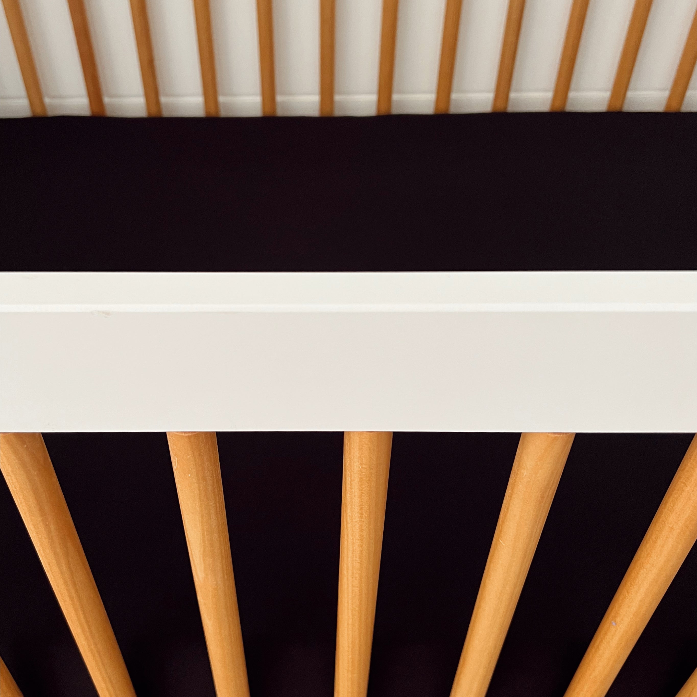 Close-up of a crib showing wooden rods and a white top rail against a dark background.