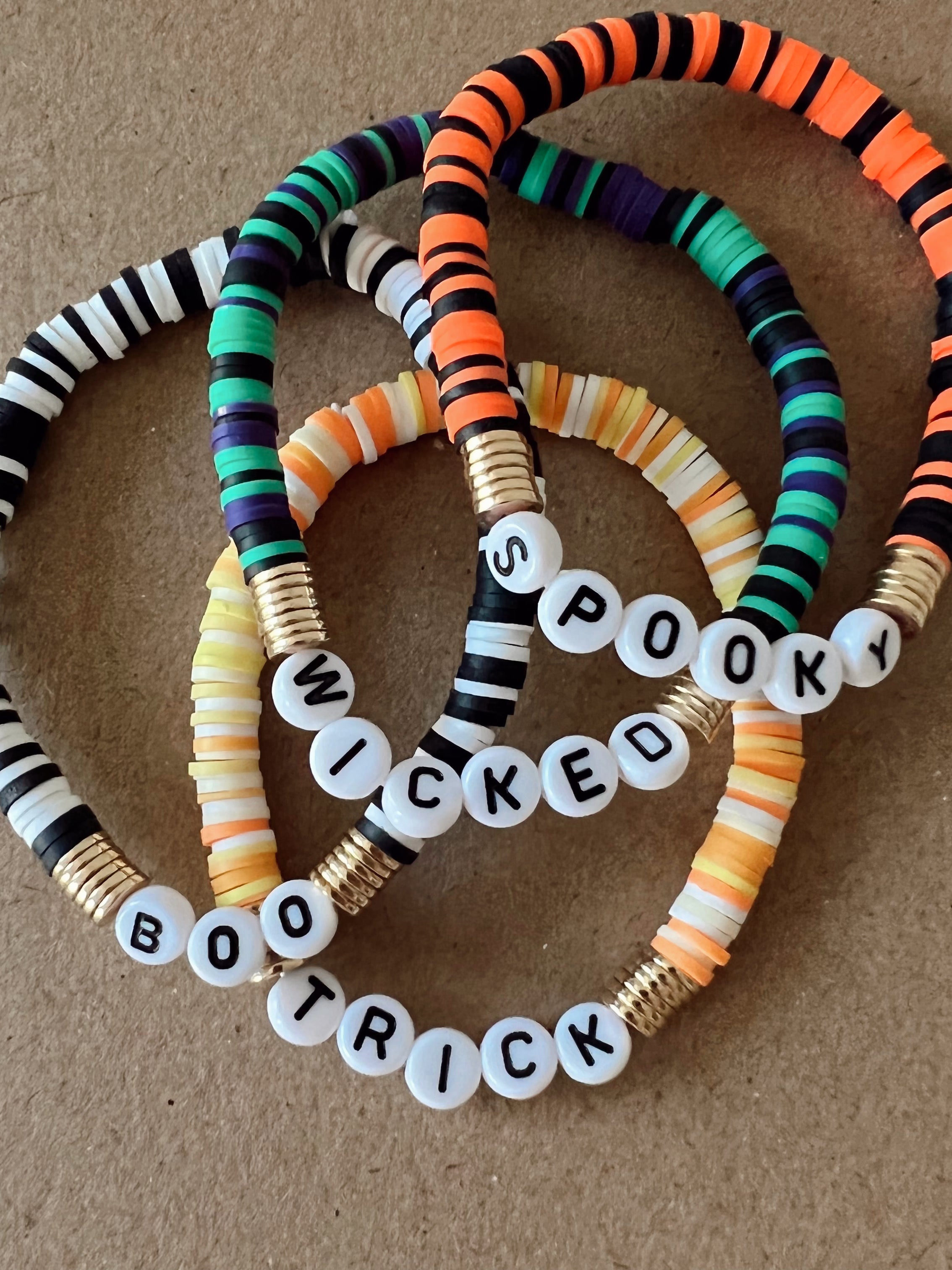 Colorful beaded bracelets with words "Spooky," "Wicked," and "Boo Trick," on a textured background.