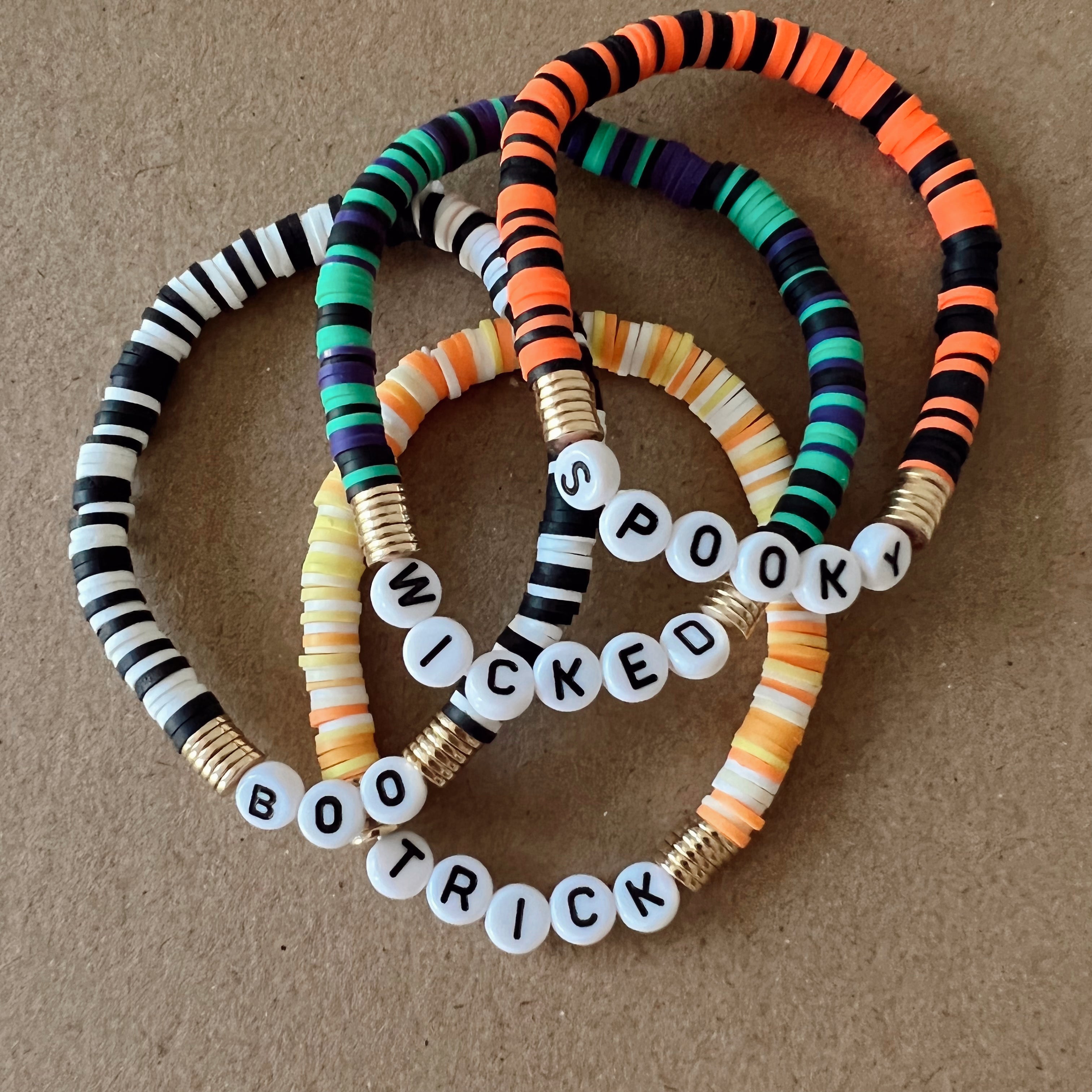 Colorful beaded bracelets with words "Spooky," "Wicked," and "Boo Trick," on a textured background.