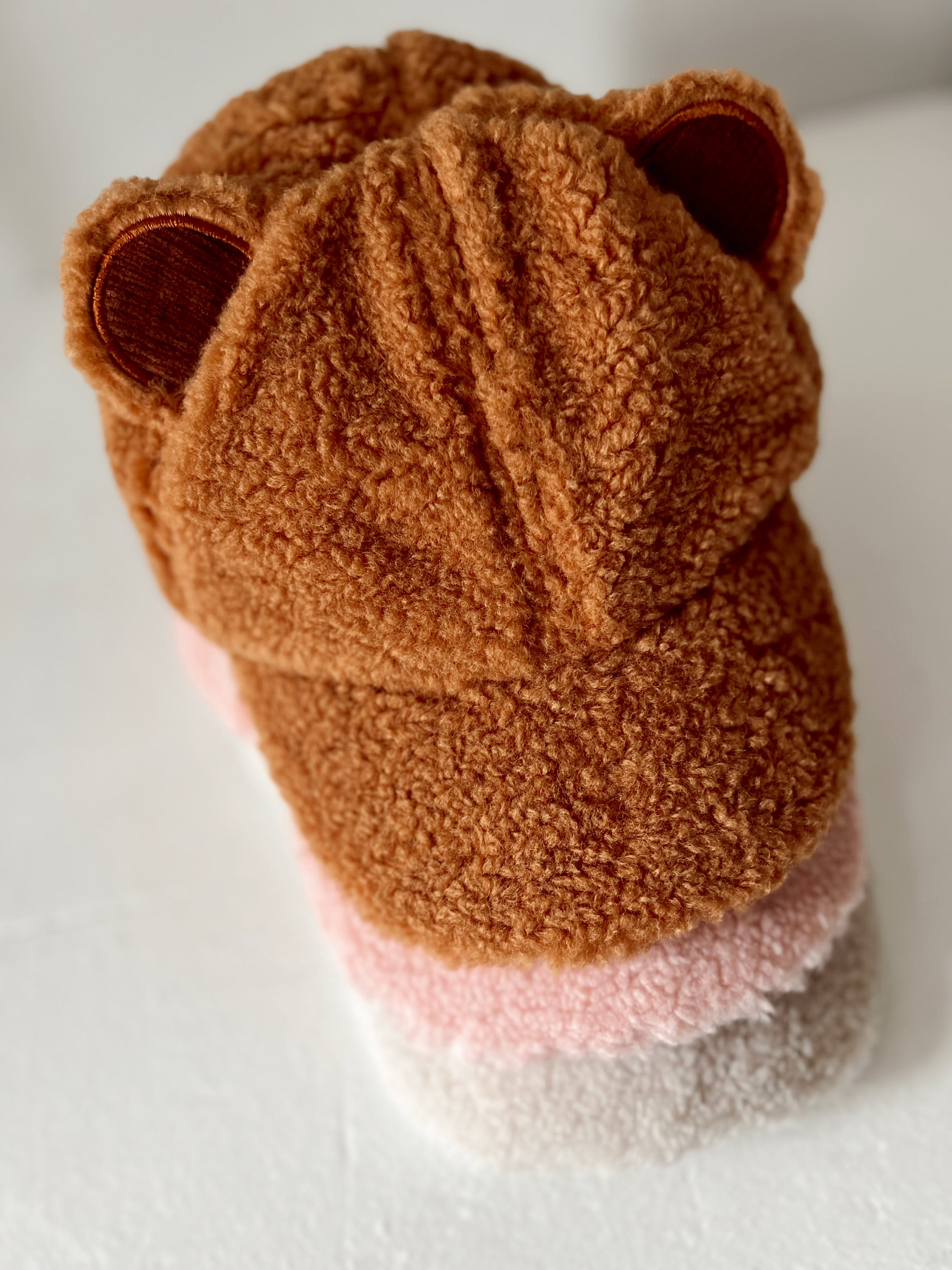 Brown bear-themed hat with fuzzy texture and ear accents, featuring a gradient of pink and cream colors.