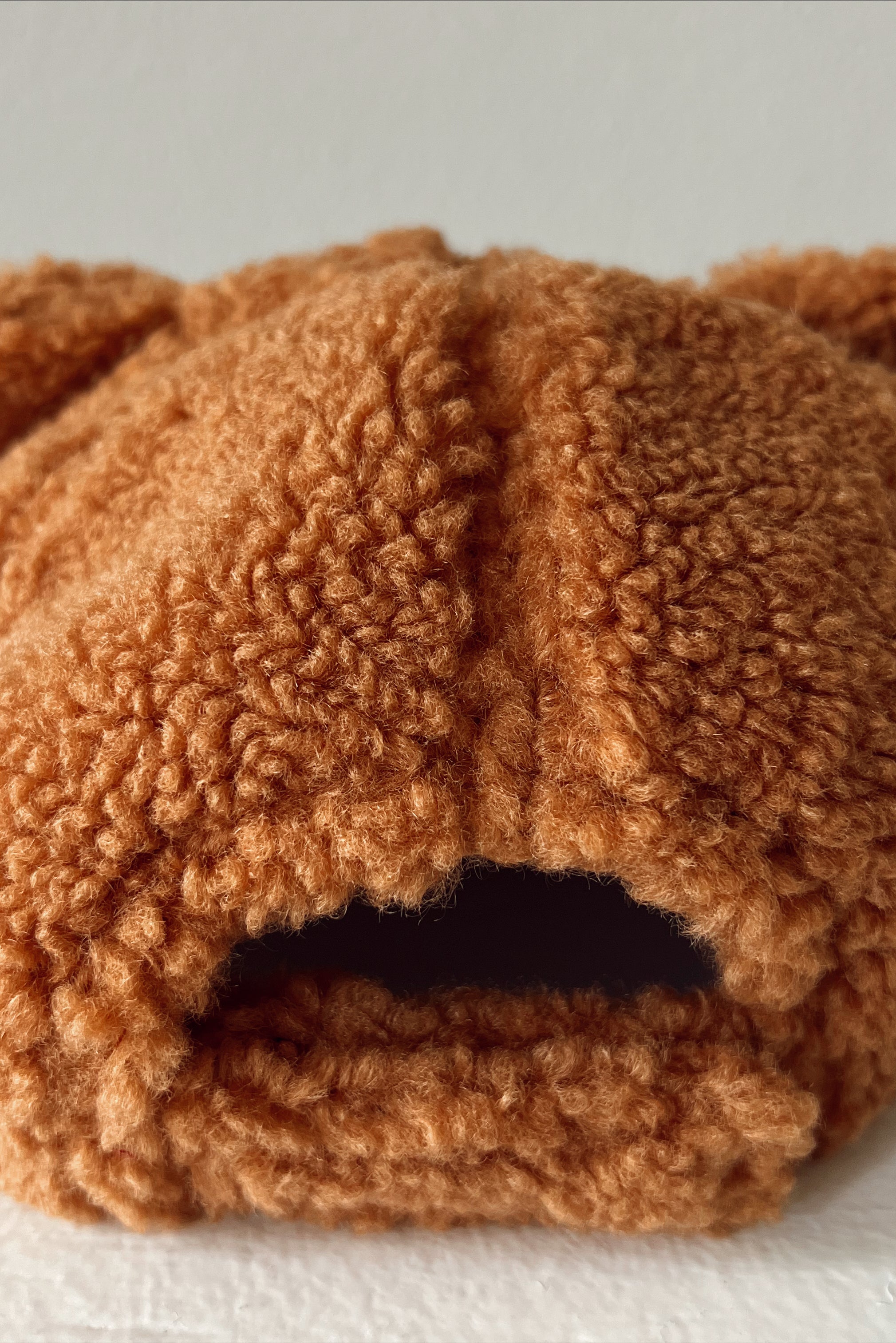 Brown bear-themed stuffed hat with fuzzy texture and ear details, viewed from the back.