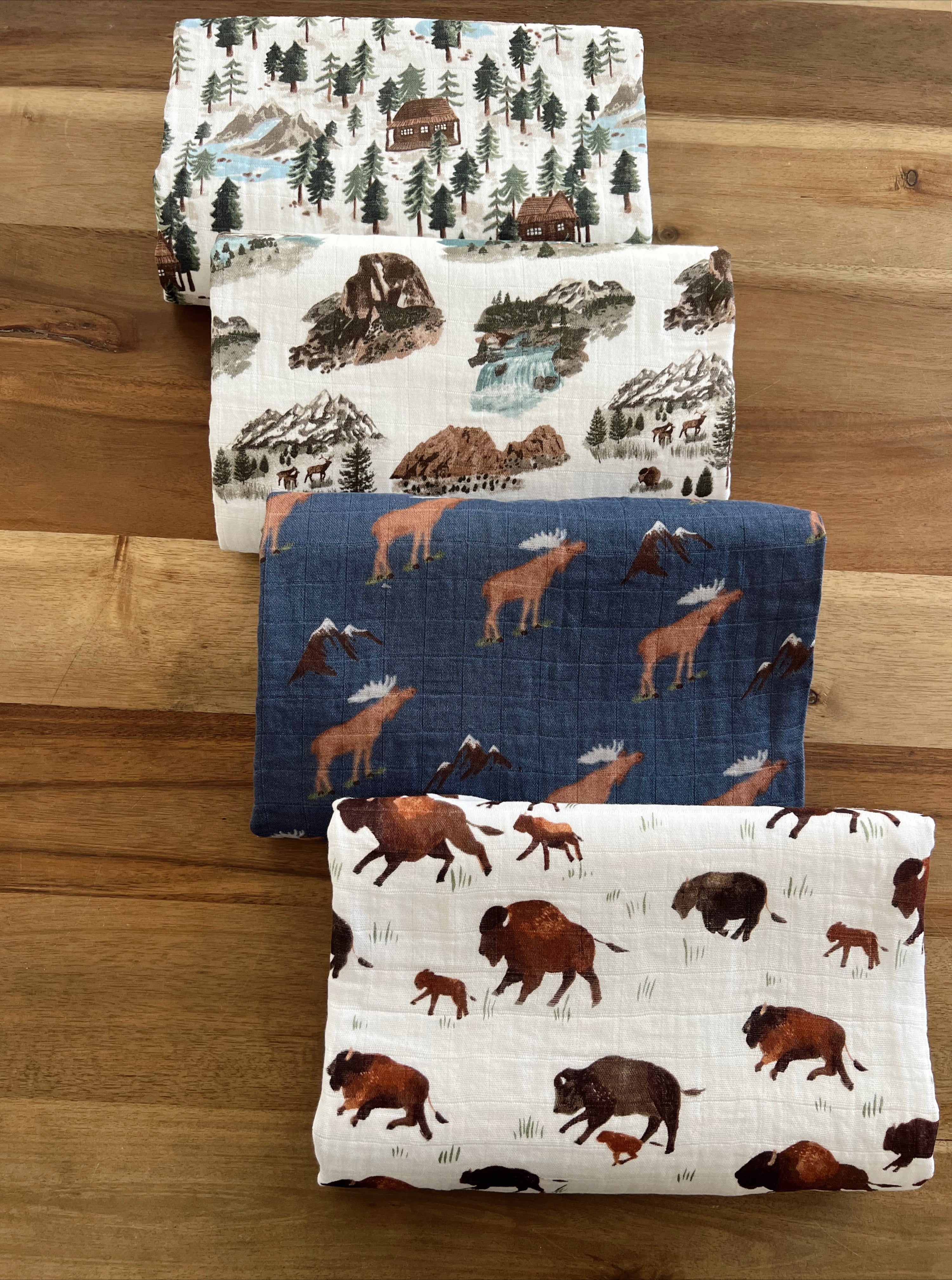 Four patterned fabric swatches featuring nature scenes, wildlife, and mountains on a wooden surface.