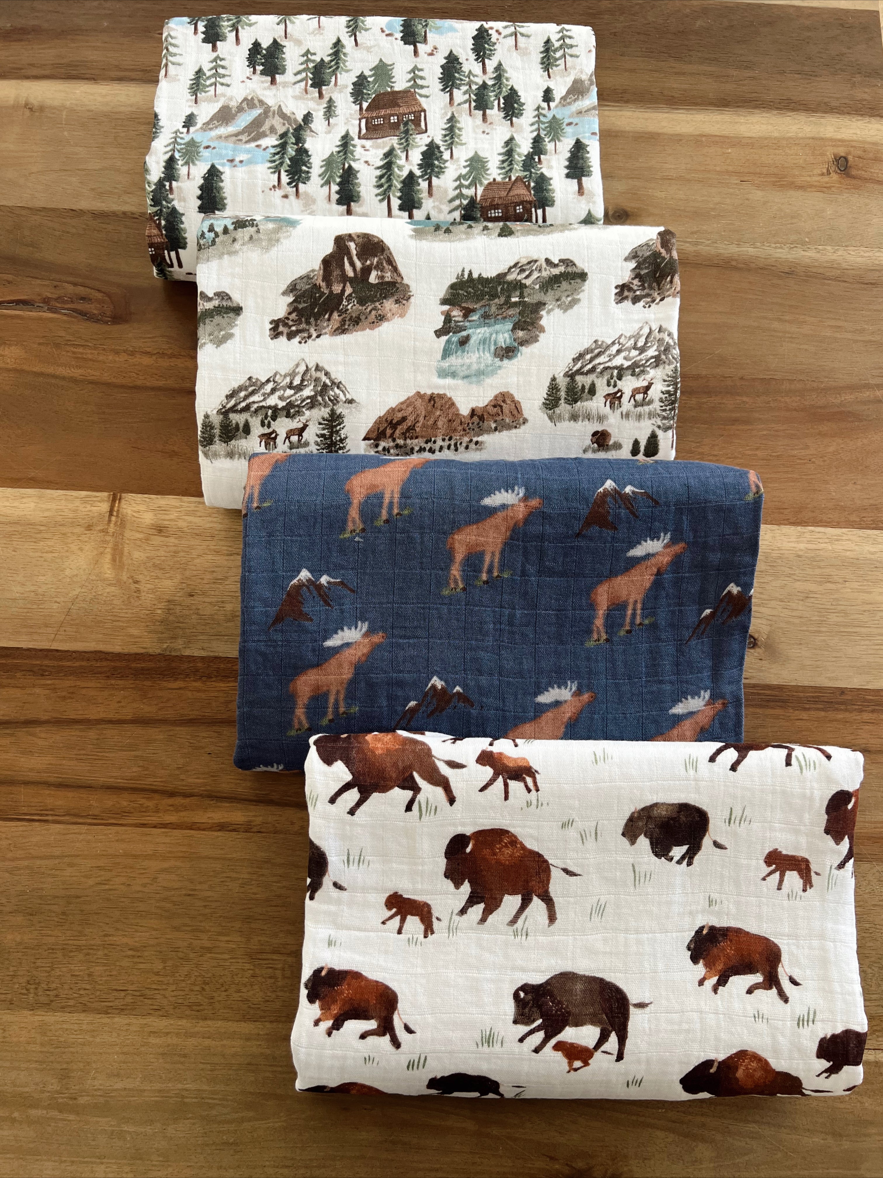 Four patterned fabric swatches featuring nature scenes, wildlife, and mountains on a wooden surface.
