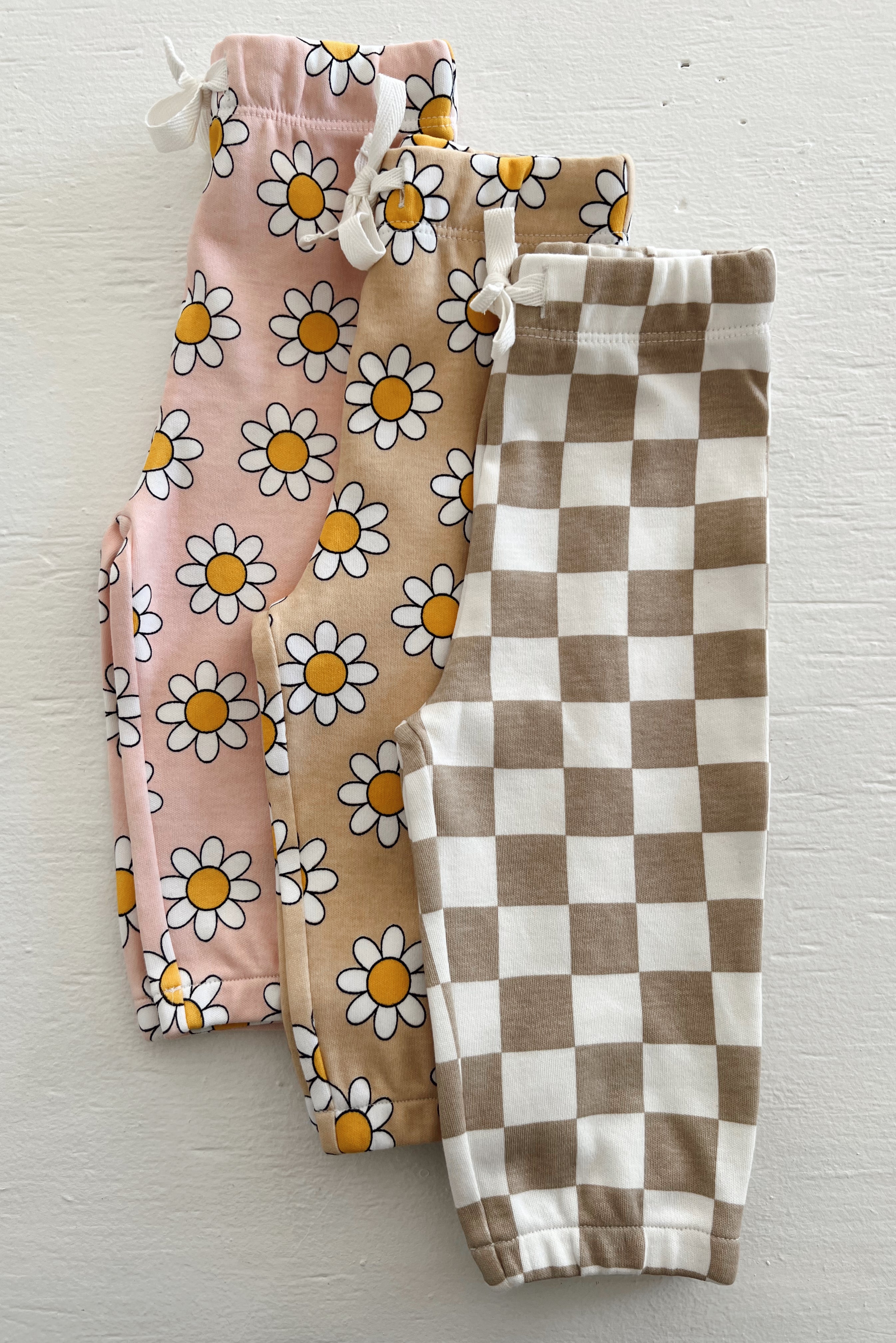 Three pairs of girl’s leggings: floral pink, beige with daisies, and brown and white checkered patterns.