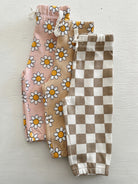 Three pairs of girl’s leggings: floral pink, beige with daisies, and brown and white checkered patterns.