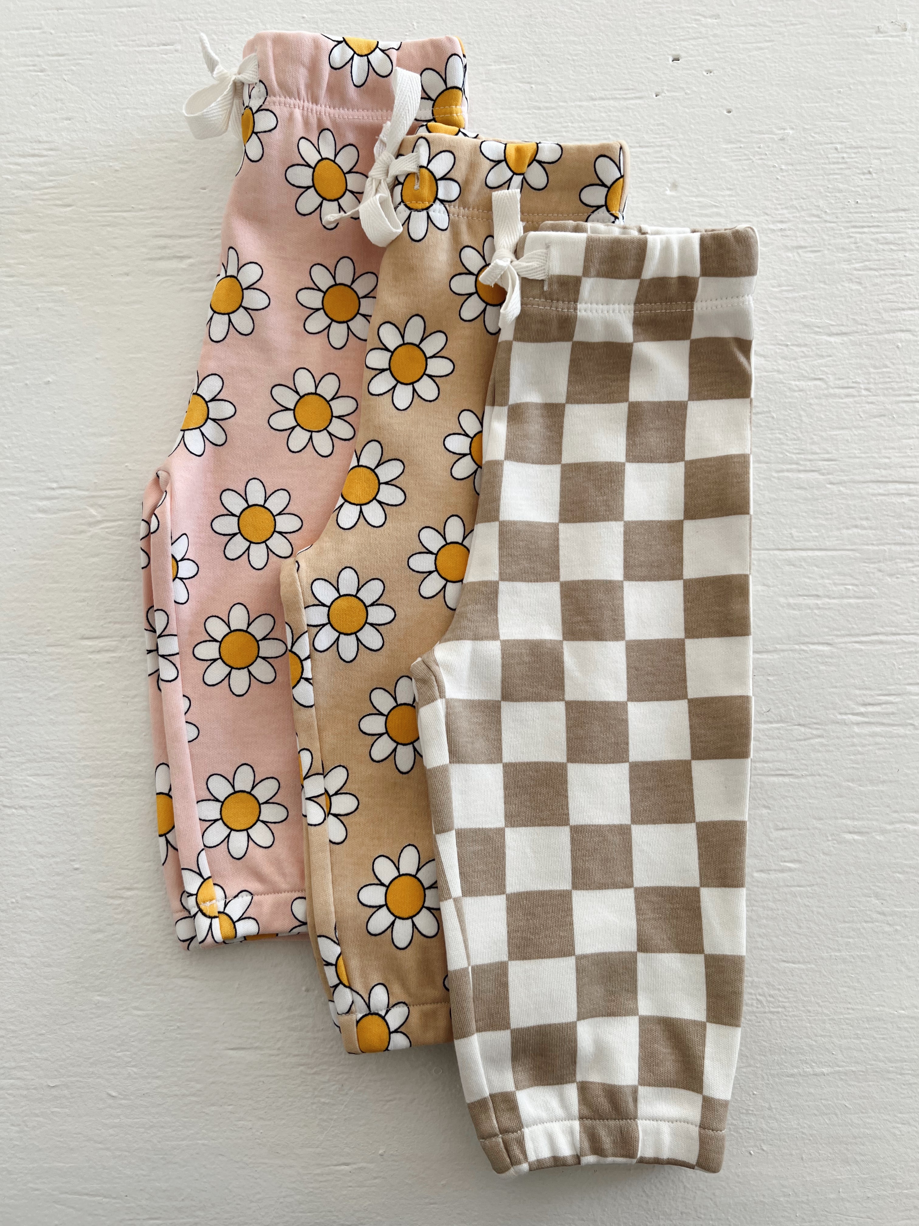 Three pairs of girl’s leggings: floral pink, beige with daisies, and brown and white checkered patterns.