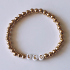 Gold bead bracelet with white letter beads spelling "LEO." Elegant and stylish accessory.