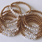 Variety of beaded bracelets displaying zodiac signs on white and gold beads.