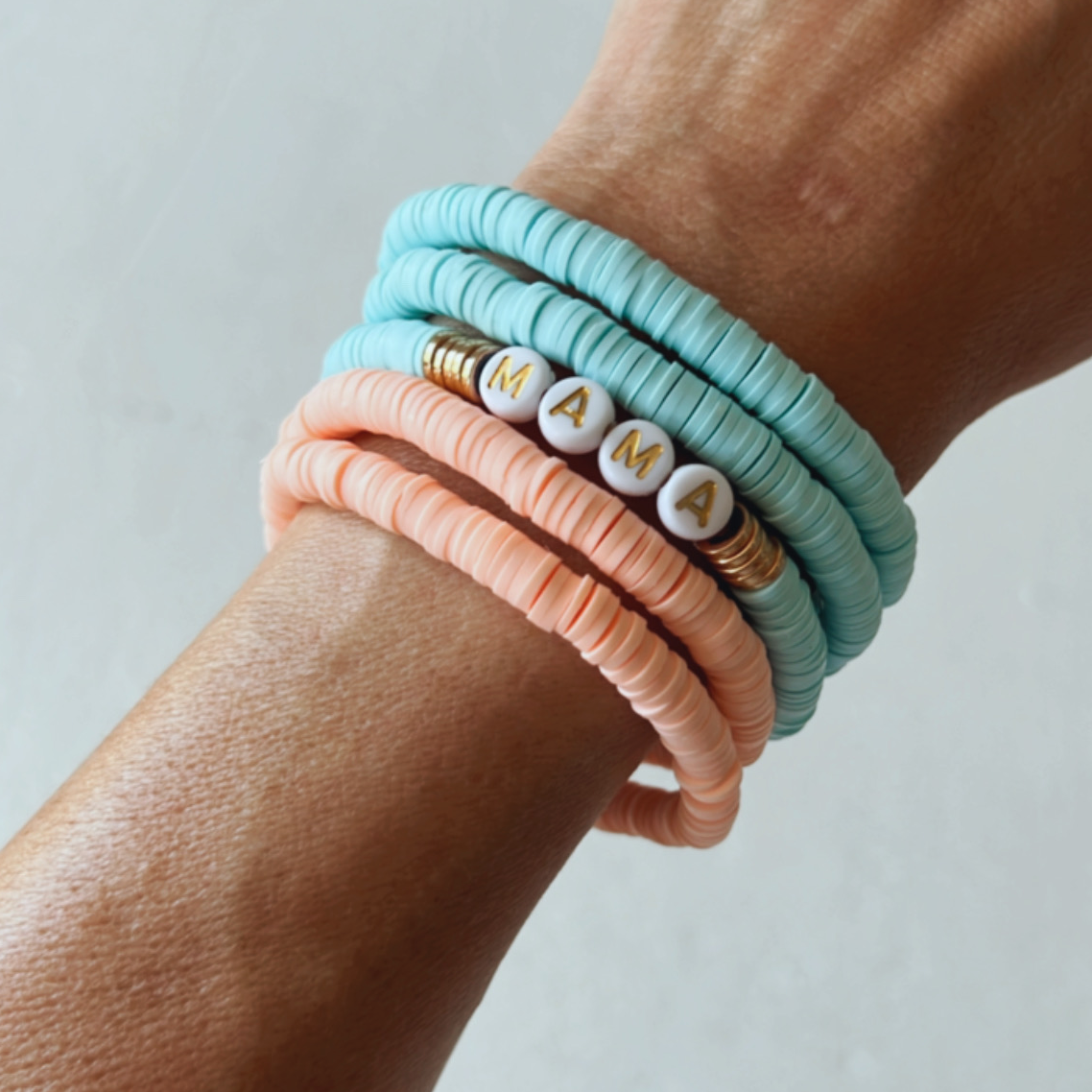 Colorful silicone bracelets stacked on a wrist, spelling "MAMA" among pastel beads.