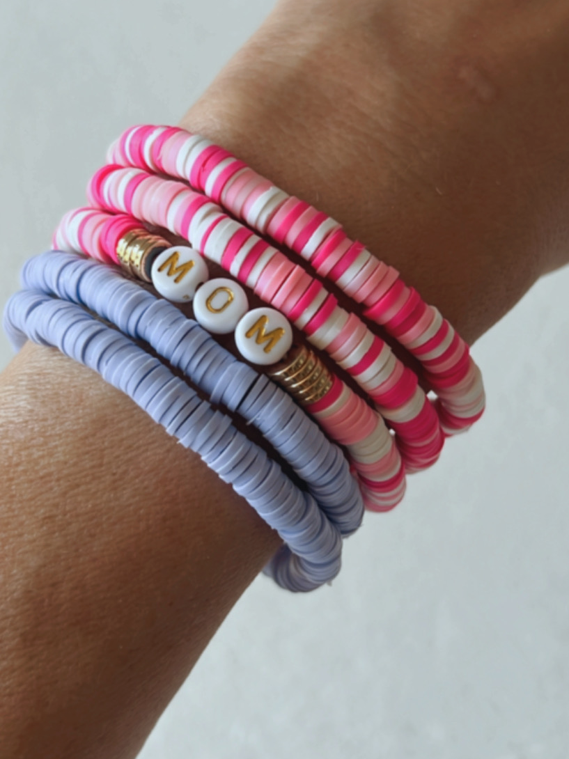 Colorful rubber bracelets stacked on a wrist, featuring a white bead with the word "MOM" in gold letters.