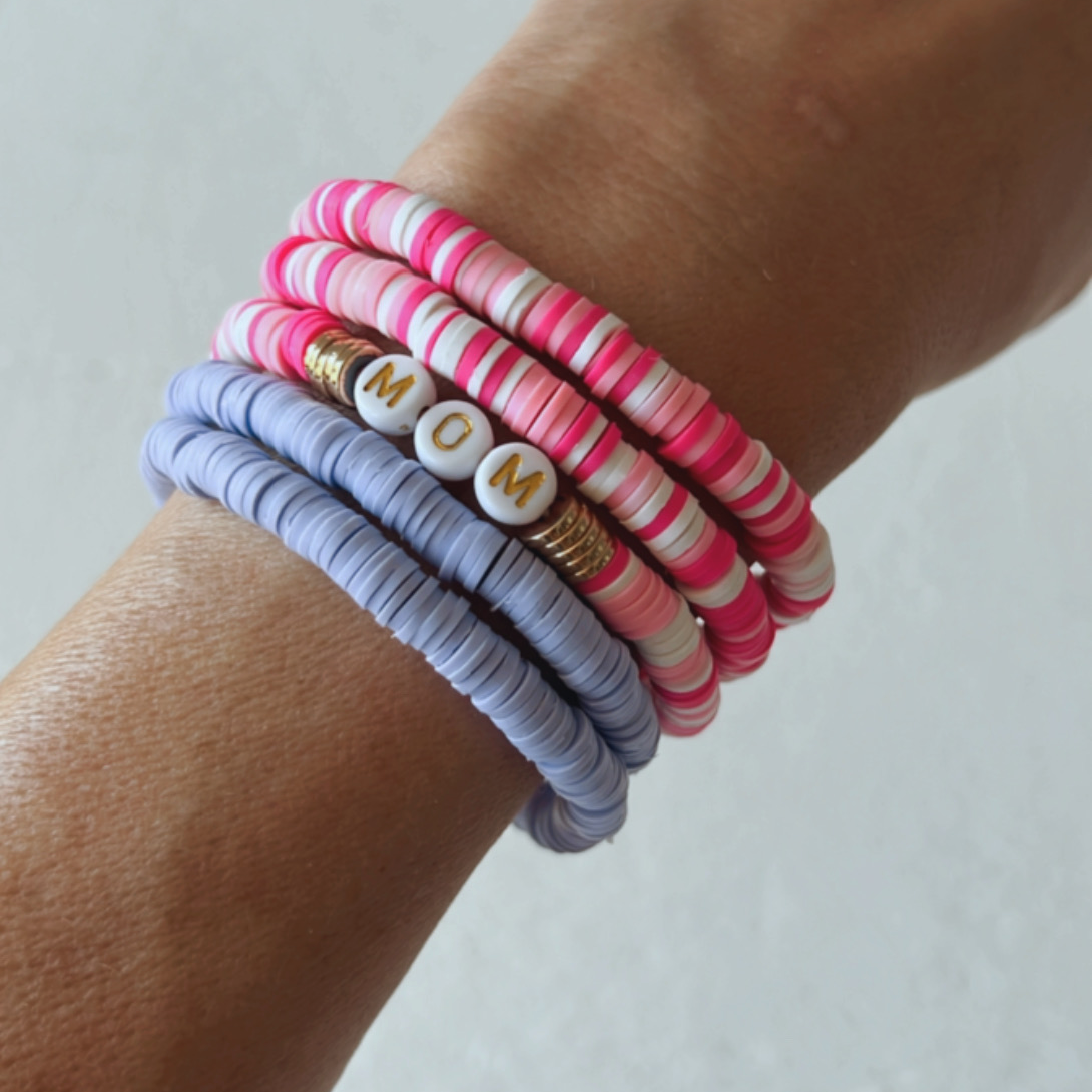 Colorful rubber bracelets stacked on a wrist, featuring a white bead with the word "MOM" in gold letters.