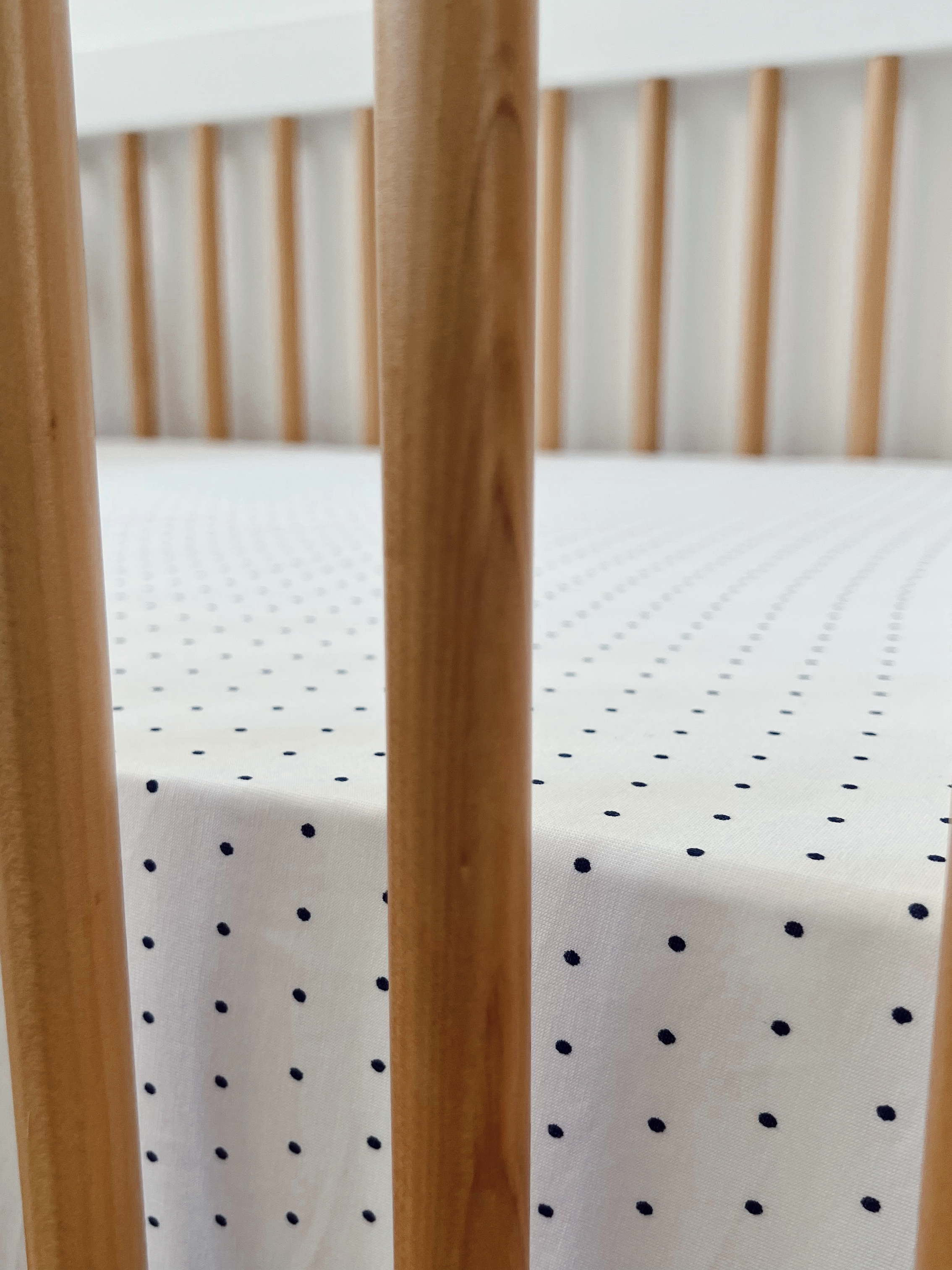 Close-up of a crib's wooden slats and a white fitted sheet with navy polka dots.