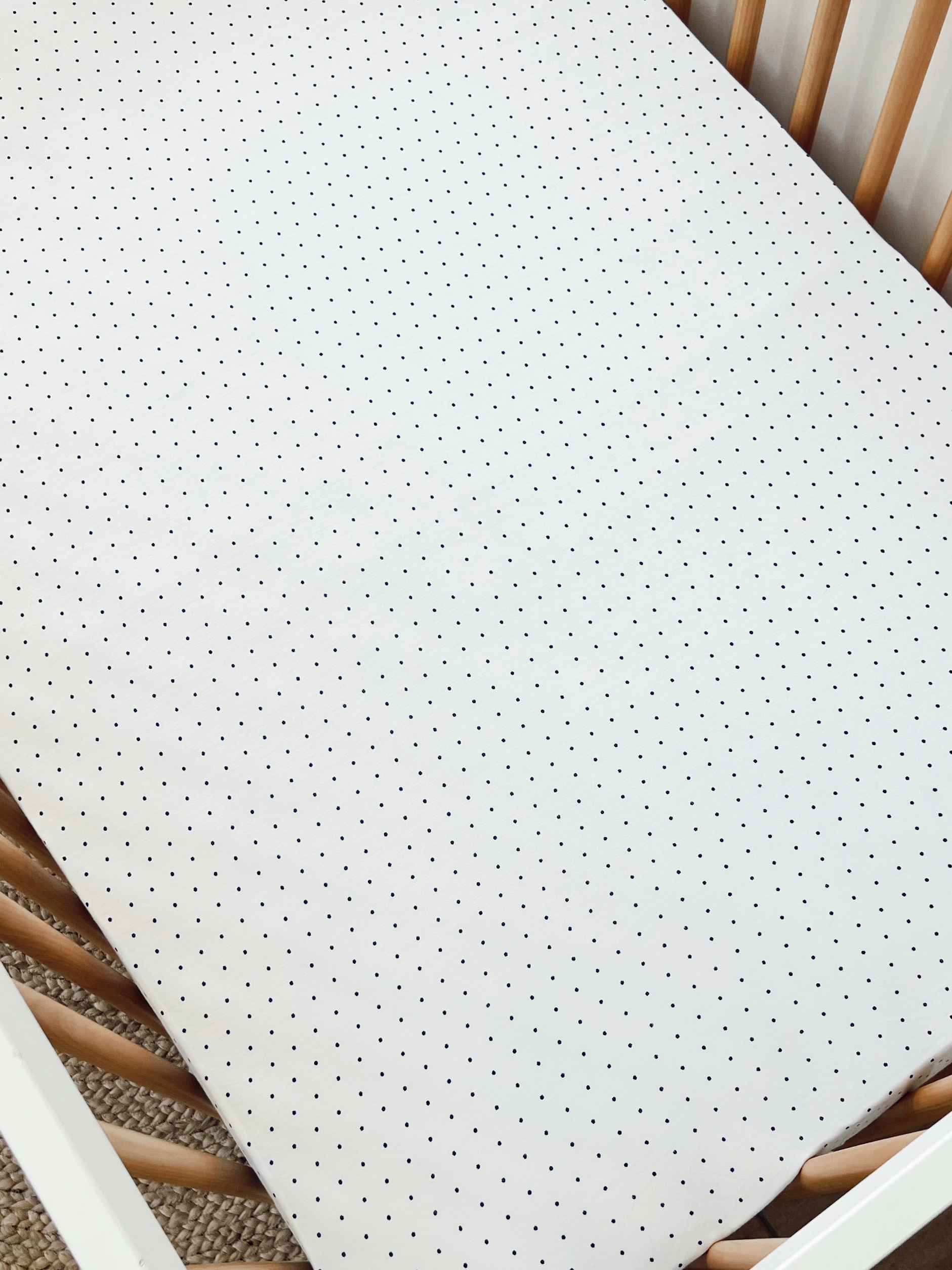 Crib mattress covered with white fabric featuring small black polka dots, surrounded by wooden crib slats.