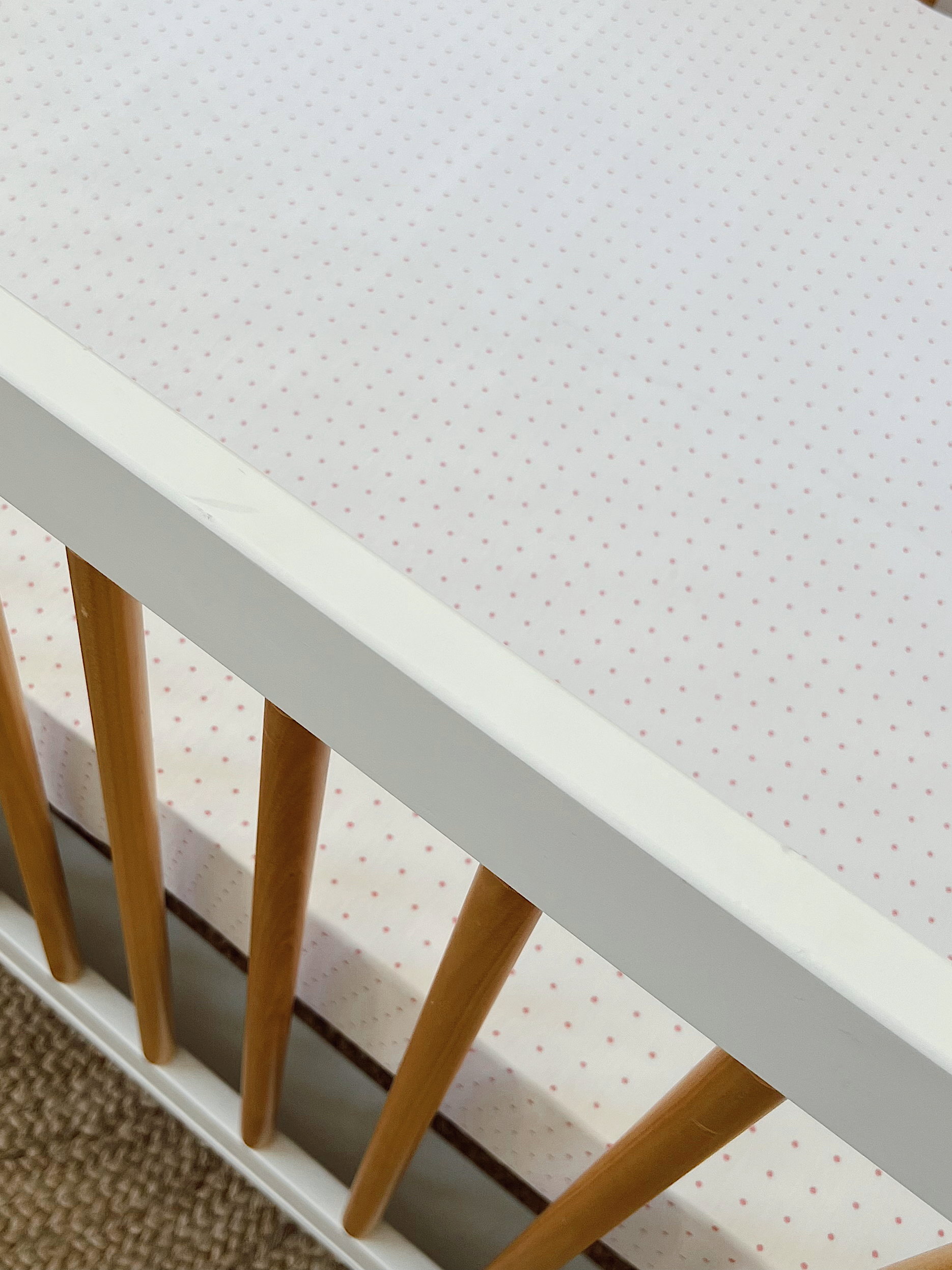 White crib with wooden slats and a polka dot mattress cover. Suitable for a nursery setting.
