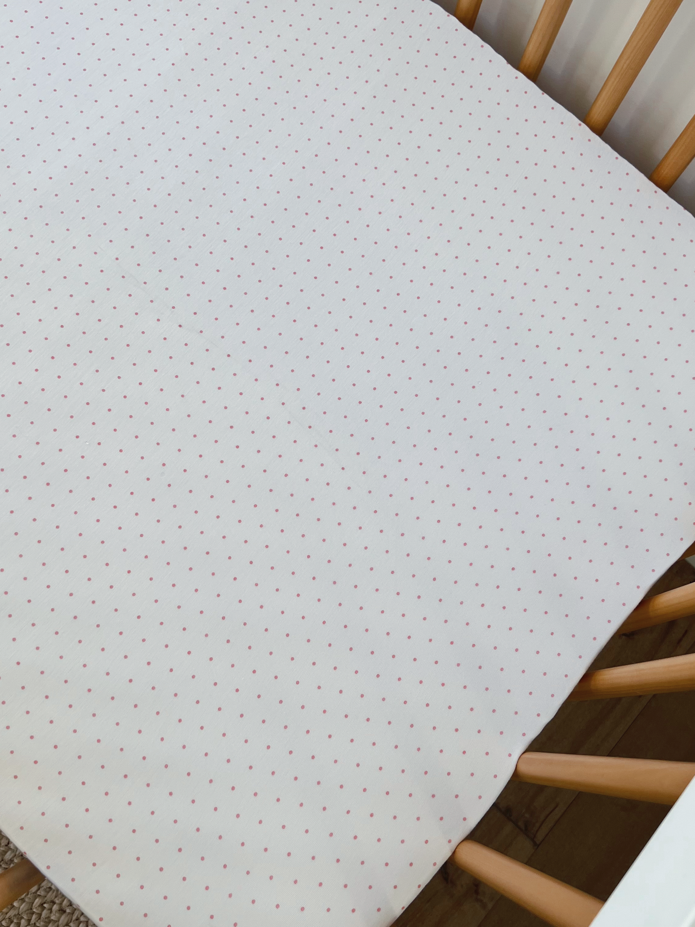 White crib mattress cover with red polka dots in a wooden crib setting.